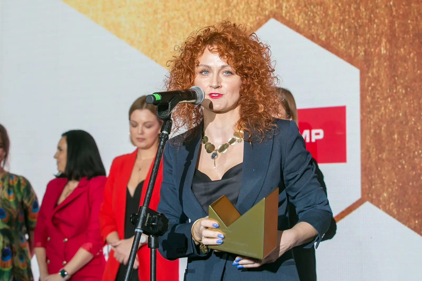Rudowłosa laureatka w granatowym garniturze z uśmiechem przemawia przy mikrofonie — Gala DMR XI (2022)