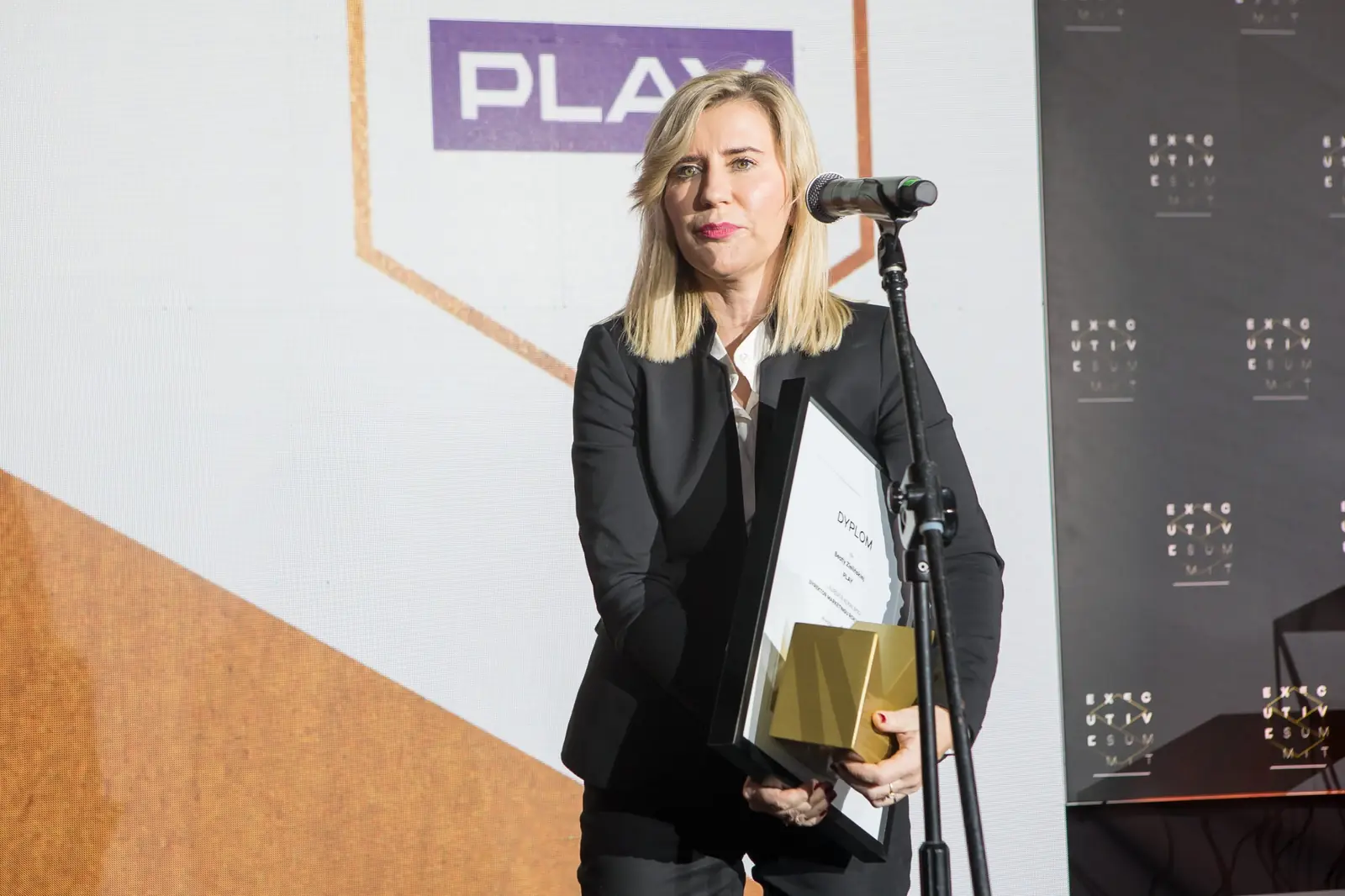 Laureatka w czarnym żakiecie przemawia przy mikrofonie, trzymając dyplom i statuetkę — Gala DMR XI (2022)