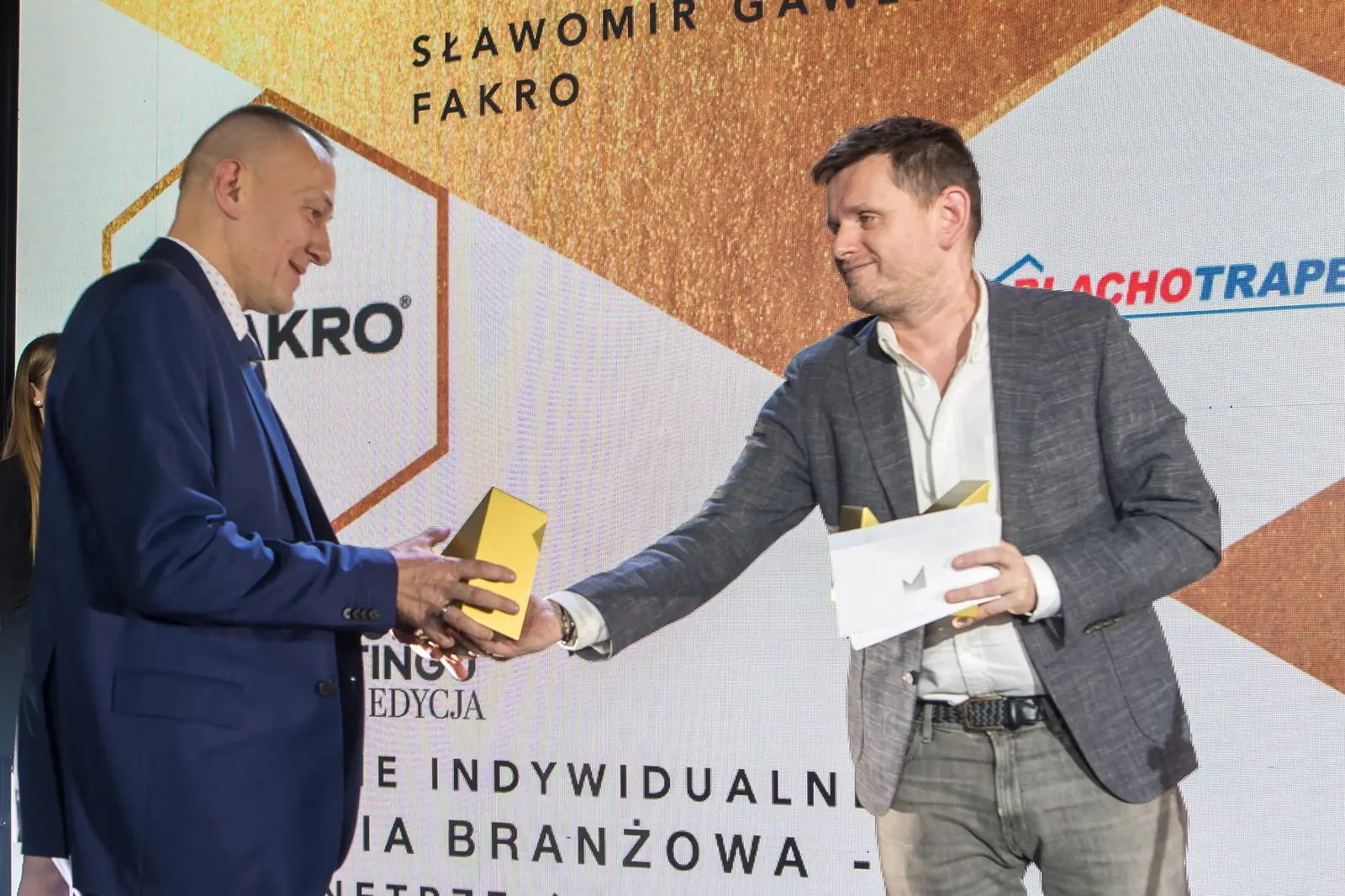 Wręczający z kopertą w dłoni przekazuje statuetkę laureatowi z kategorii dom i budownictwo — Gala DMR XI (2022)