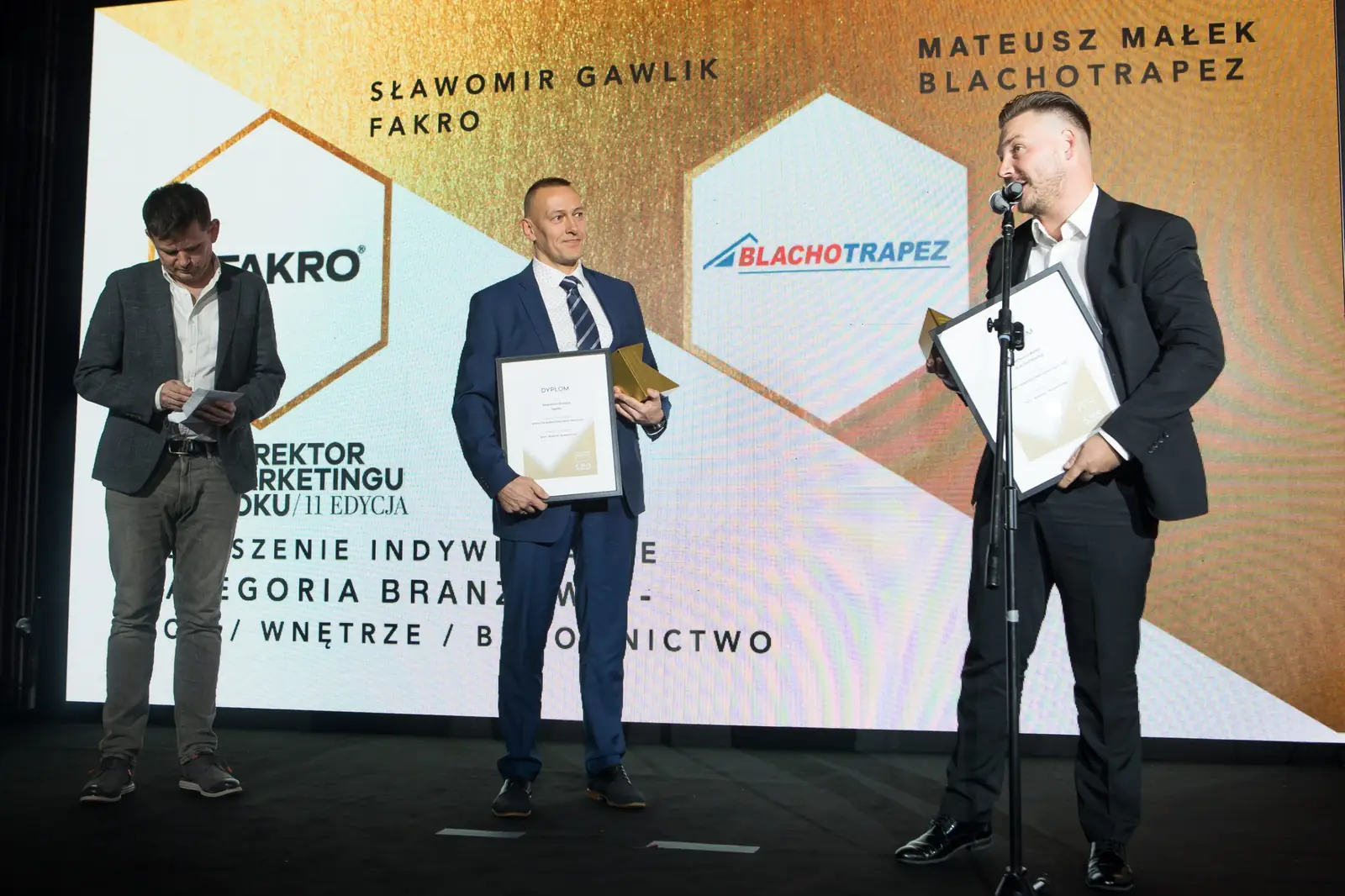 Szeroki kadr sceny: jeden laureat przemawia przy mikrofonie, drugi czeka obok z dyplomem — Gala DMR XI (2022)