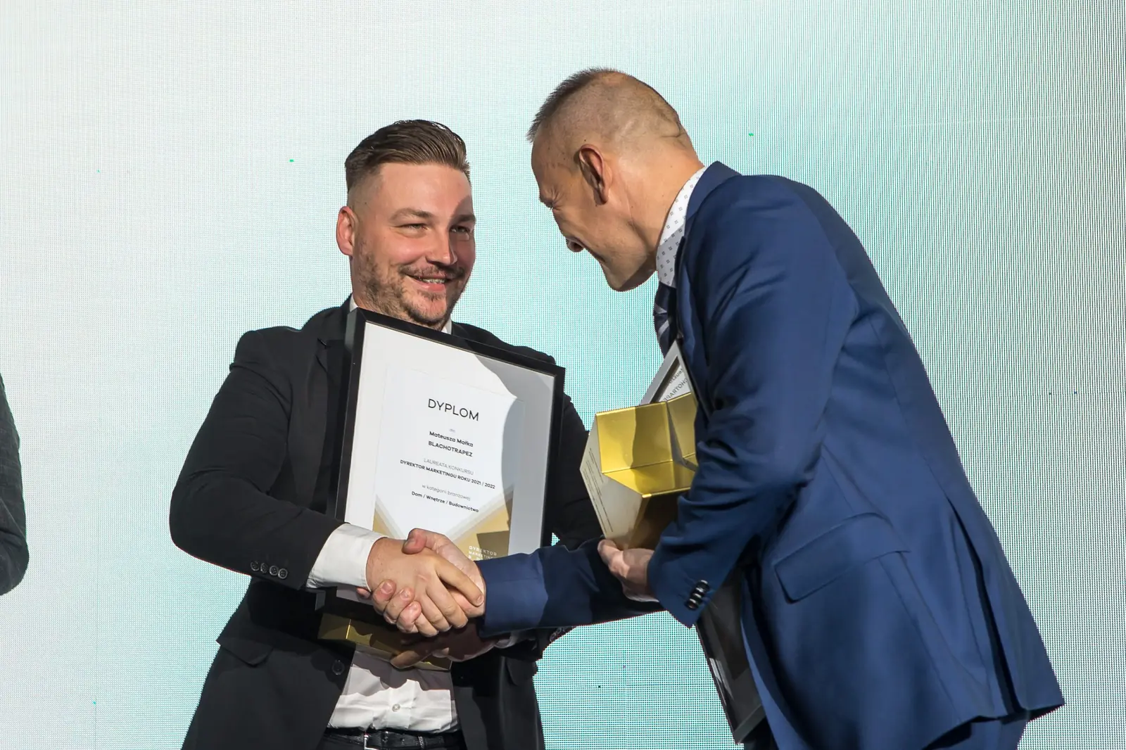 Two winners congratulate each other with a handshake, one holding a diploma, the other a statuette — DMR Gala XI (2022)