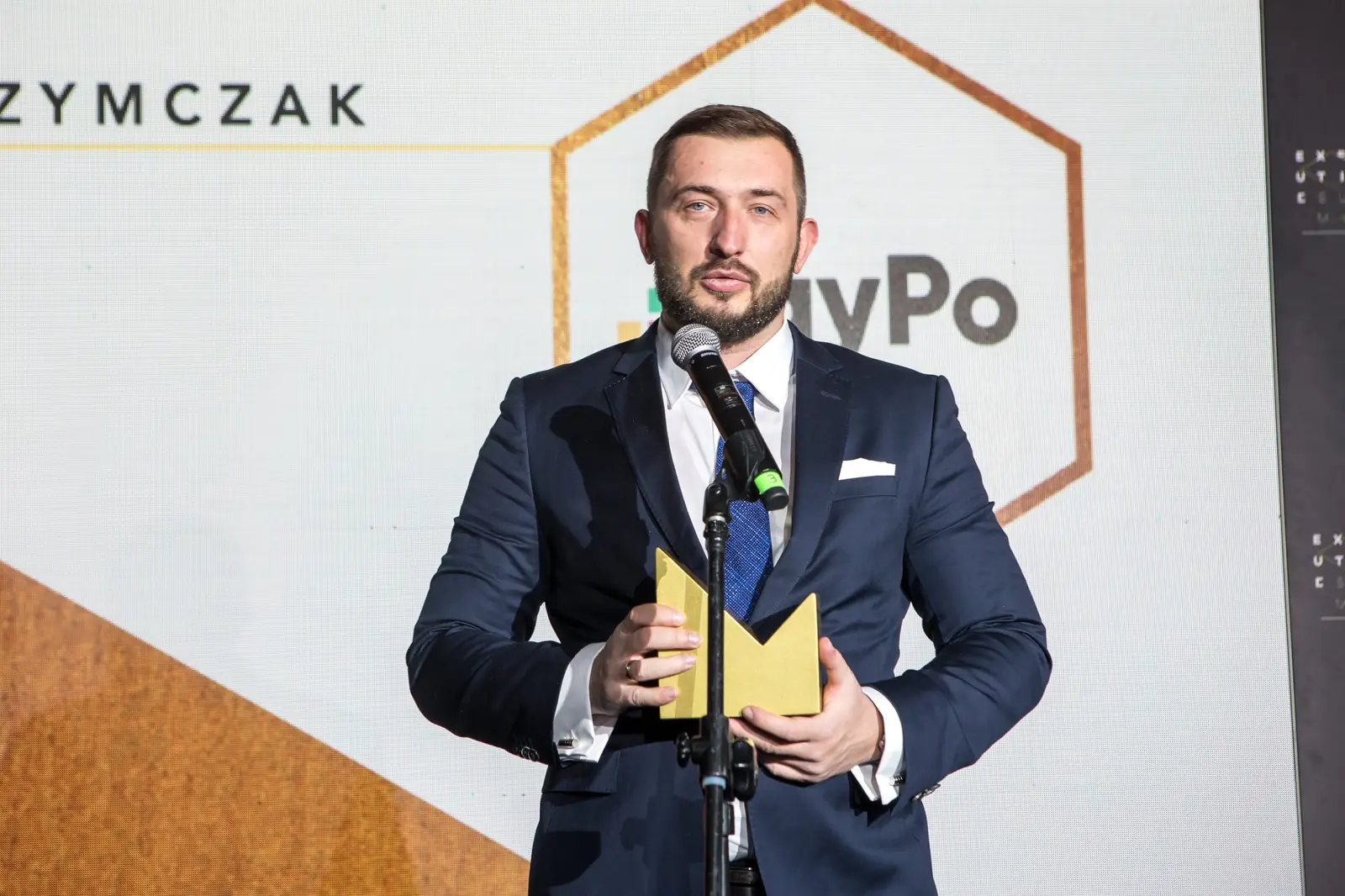 Laureat z krótką brodą przemawia przy mikrofonie, trzymając złotą statuetkę przed sobą — Gala DMR XI (2022)