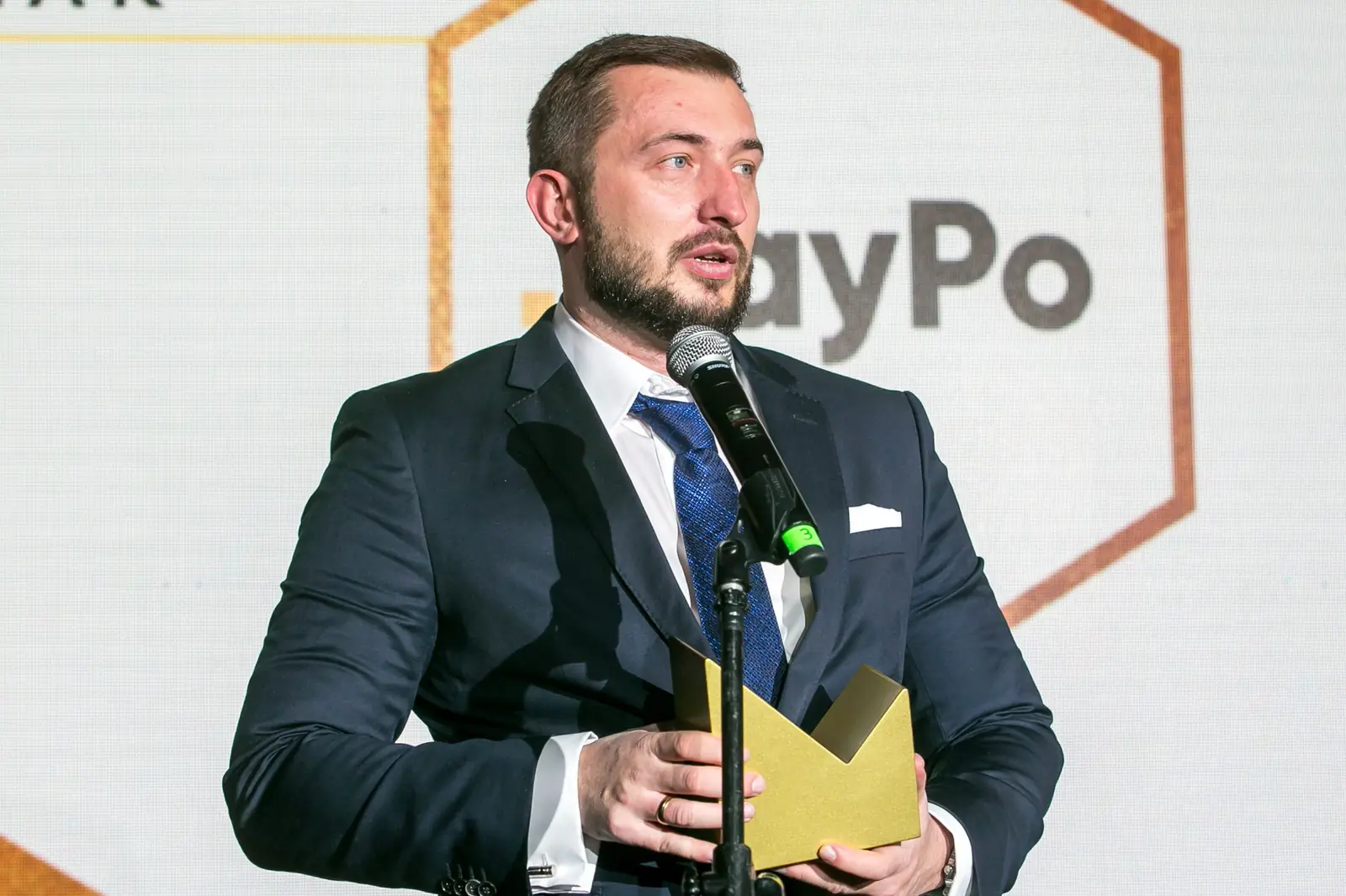 Zbliżenie na laureata w granatowym garniturze, który mówi do mikrofonu ze statuetką w dłoniach — Gala DMR XI (2022)