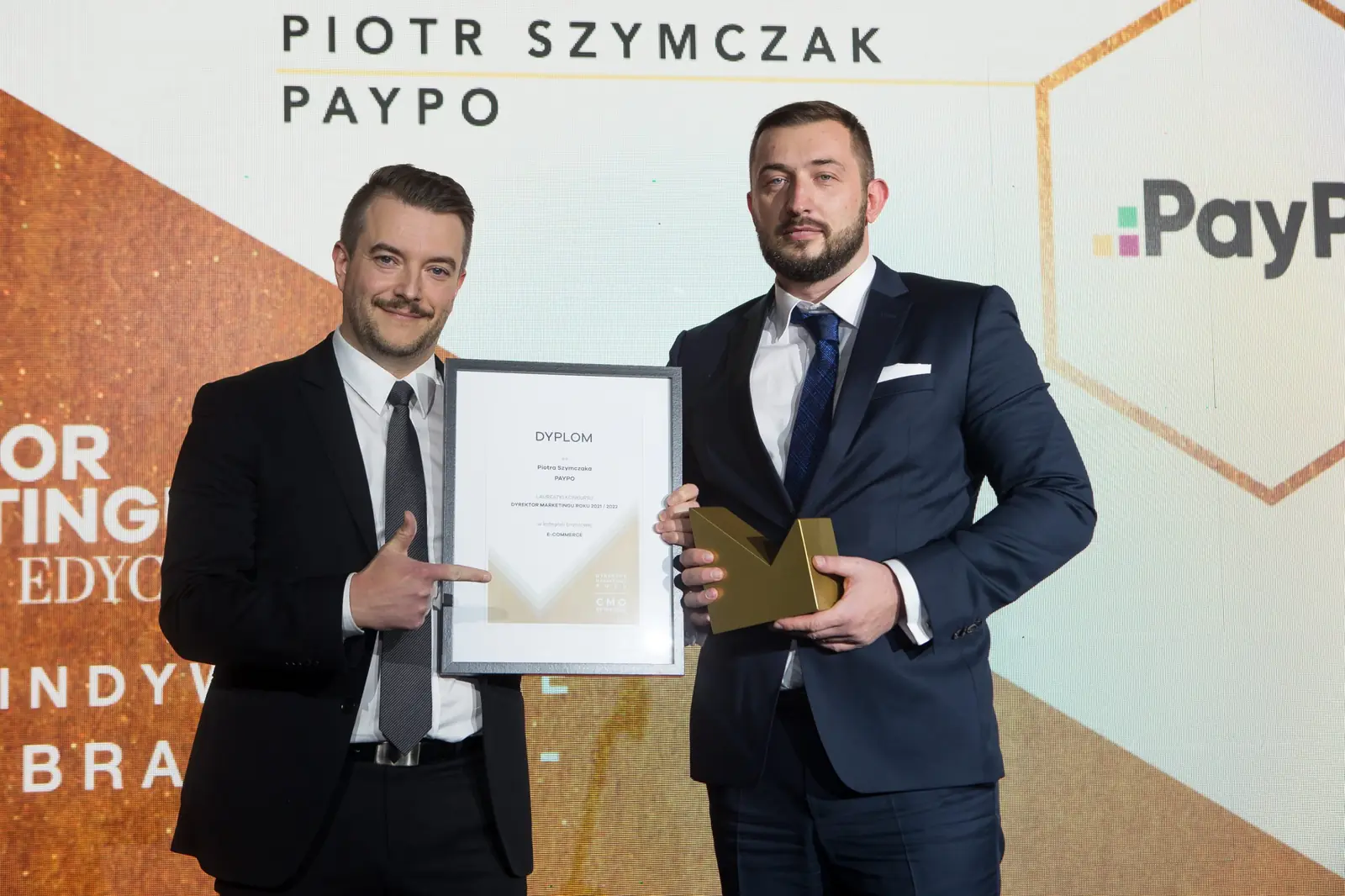 Laureat ze statuetką i dyplomem pozuje obok mężczyzny z wąsem, który wskazuje nagrodę — Gala DMR XI (2022)