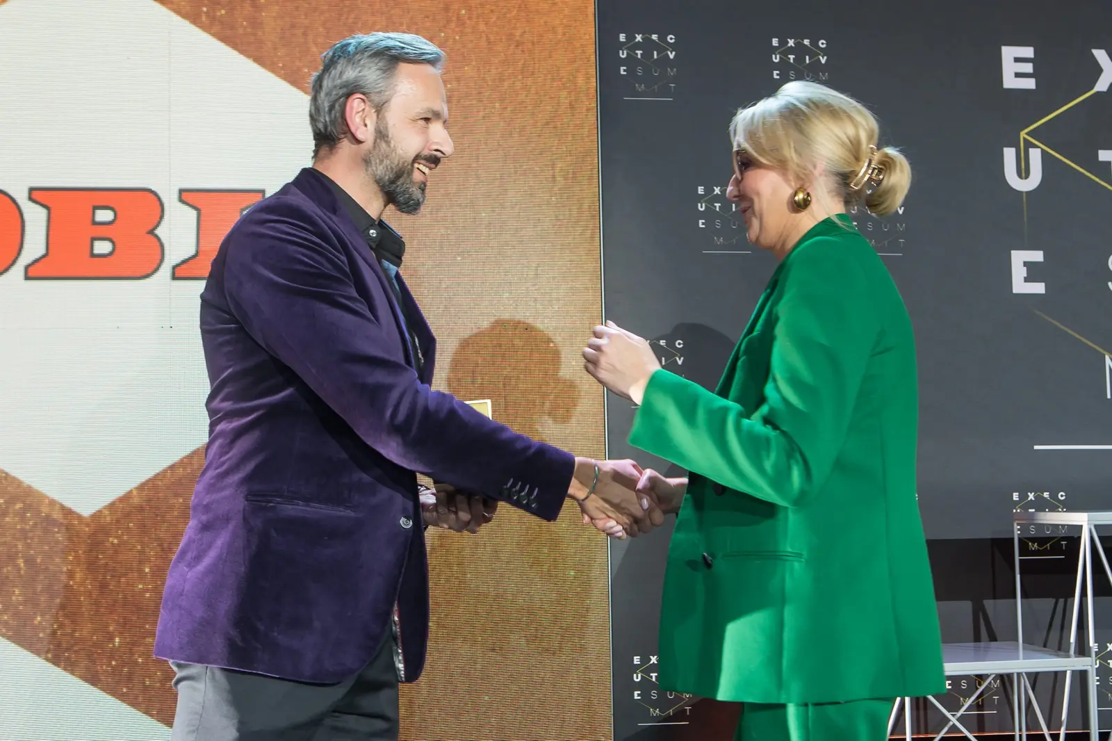 Wręczający w fioletowej marynarce ściska dłoń laureatki w zielonym garniturze — Gala DMR XI (2022)