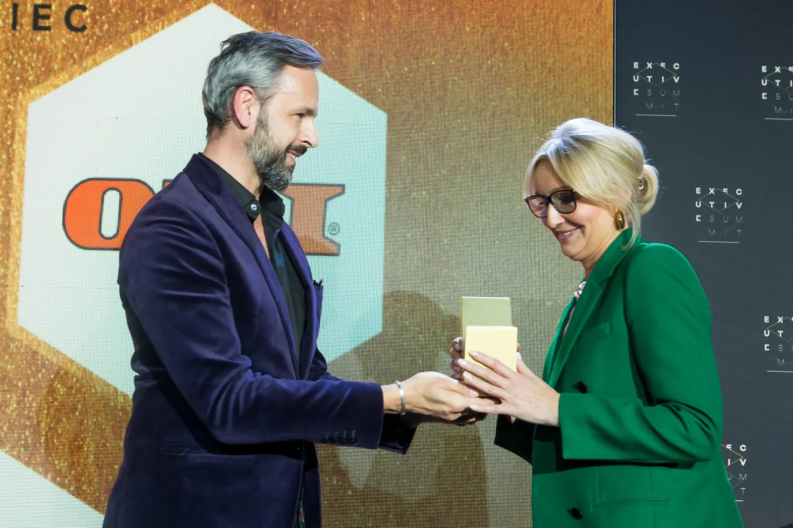 Laureatka w zielonym garniturze i okularach odbiera statuetkę od mężczyzny w fioletowej marynarce — Gala DMR XI (2022)
