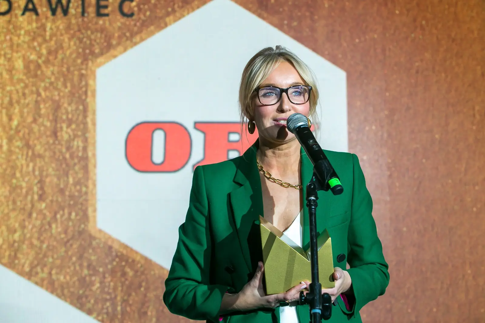 Laureatka w zielonym garniturze przemawia do mikrofonu, przyciskając do siebie złotą statuetkę — Gala DMR XI (2022)