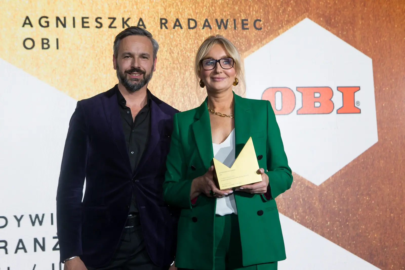 Laureatka w zielonym garniturze pozuje ze statuetką obok wręczającego w fioletowej marynarce — Gala DMR XI (2022)