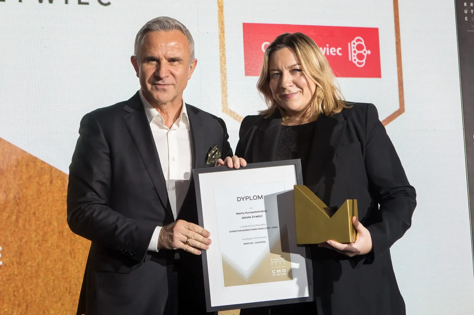 Laureatka z dyplomem i statuetką pozuje ze szpakowatym mężczyzną w ciemnym garniturze — Gala DMR XI (2022)