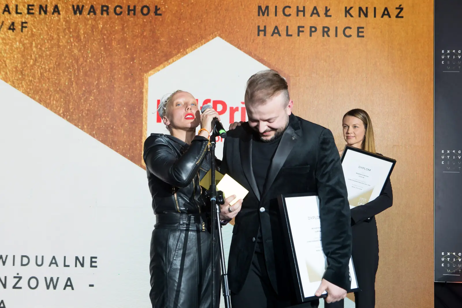 Kobieta z białymi dredami serdecznie obejmuje laureata z dyplomem, w tle druga laureatka — Gala DMR XI (2022)