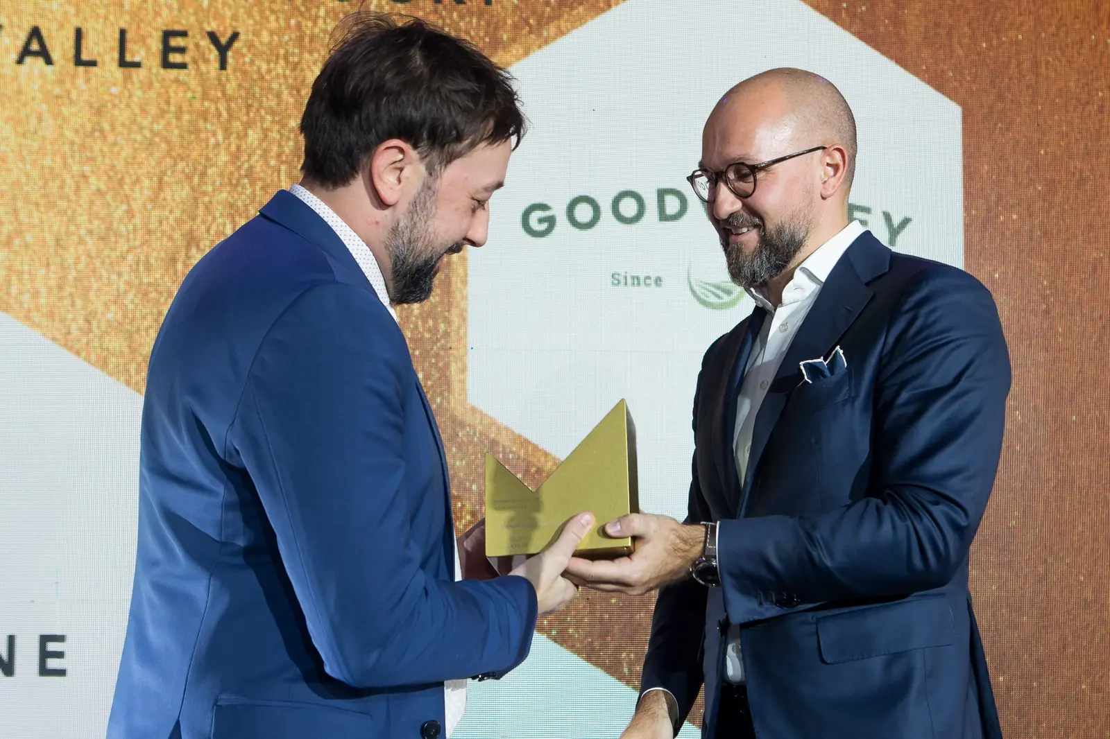 Wręczający w okularach podaje złotą statuetkę laureatowi w niebieskim garniturze — Gala DMR XI (2022)