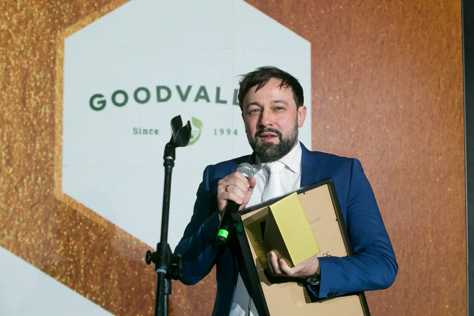 Laureat w niebieskim garniturze z uśmiechem mówi do mikrofonu, trzymając dyplom i statuetkę — Gala DMR XI (2022)