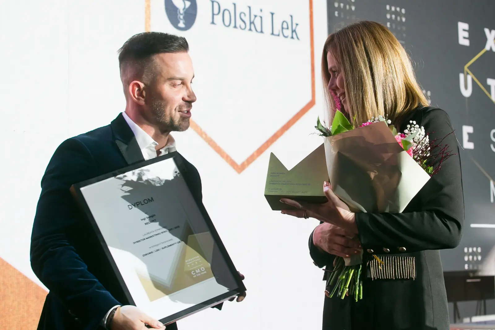 Laureatka z bukietem i statuetką spogląda na kwiaty, a wręczający trzyma jej dyplom — Gala DMR XI (2022)