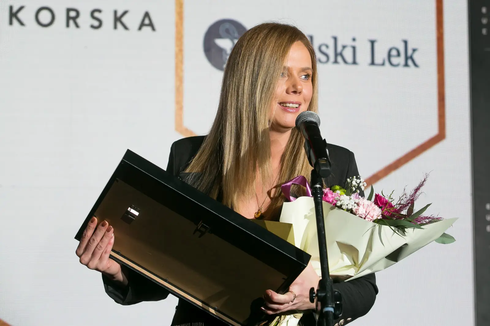 Laureatka o długich włosach przemawia z oprawionym dyplomem i bukietem kwiatów w dłoniach — Gala DMR XI (2022)