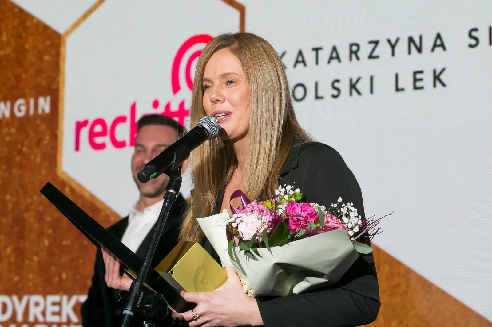 Laureatka z kwiatami i statuetką dziękuje do mikrofonu na tle czerwonego logo — Gala DMR XI (2022)