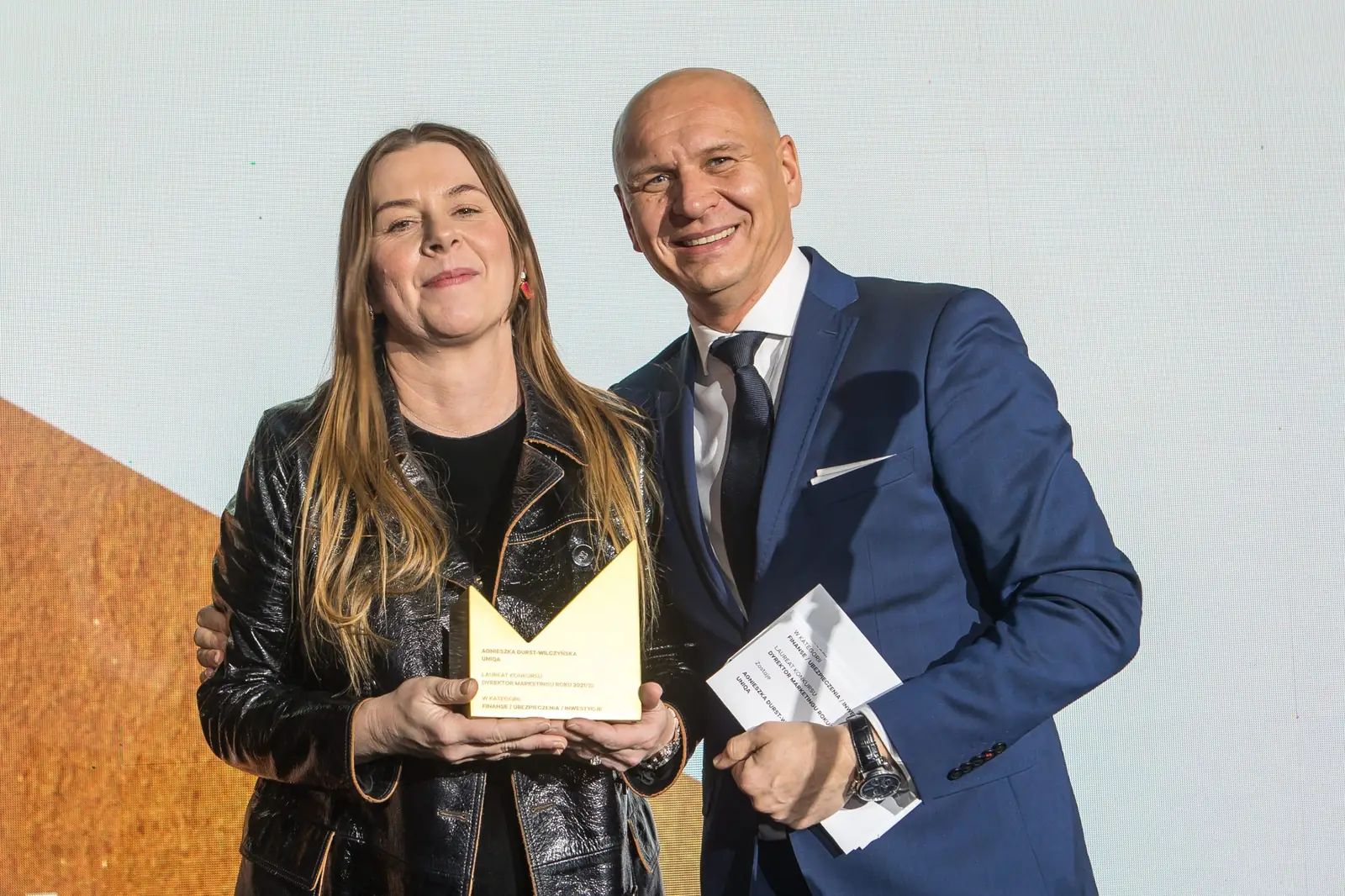 Laureatka w skórzanej kurtce trzyma statuetkę obok uśmiechniętego wręczającego — Gala DMR XI (2022)