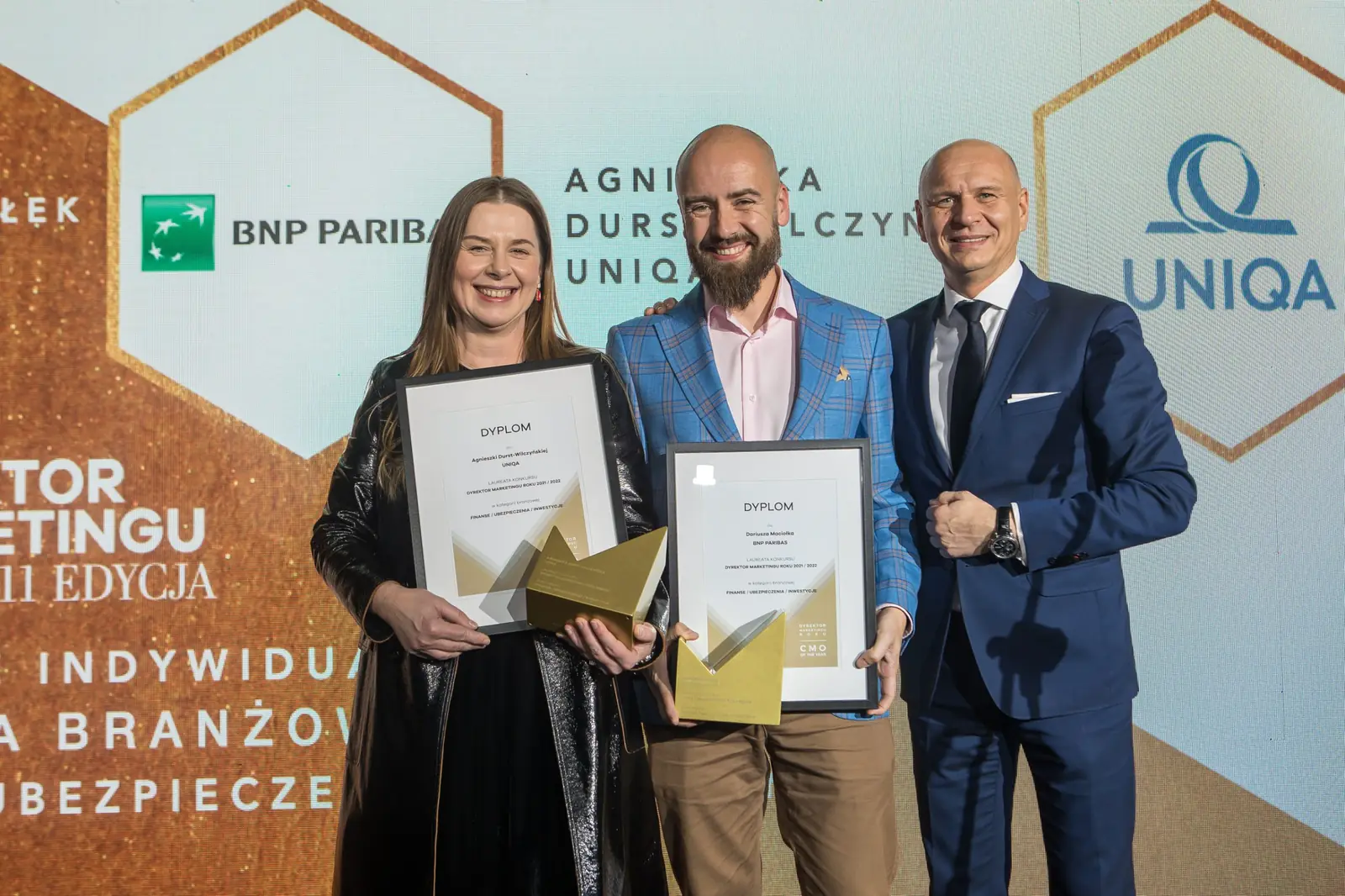 Dwoje laureatów z dyplomami i statuetkami pozuje z wręczającym w granatowym garniturze — Gala DMR XI (2022)