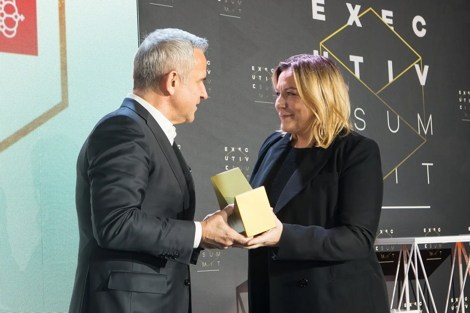 Szpakowaty mężczyzna w ciemnym garniturze wręcza statuetkę laureatce w czarnej marynarce — Gala DMR XI (2022)
