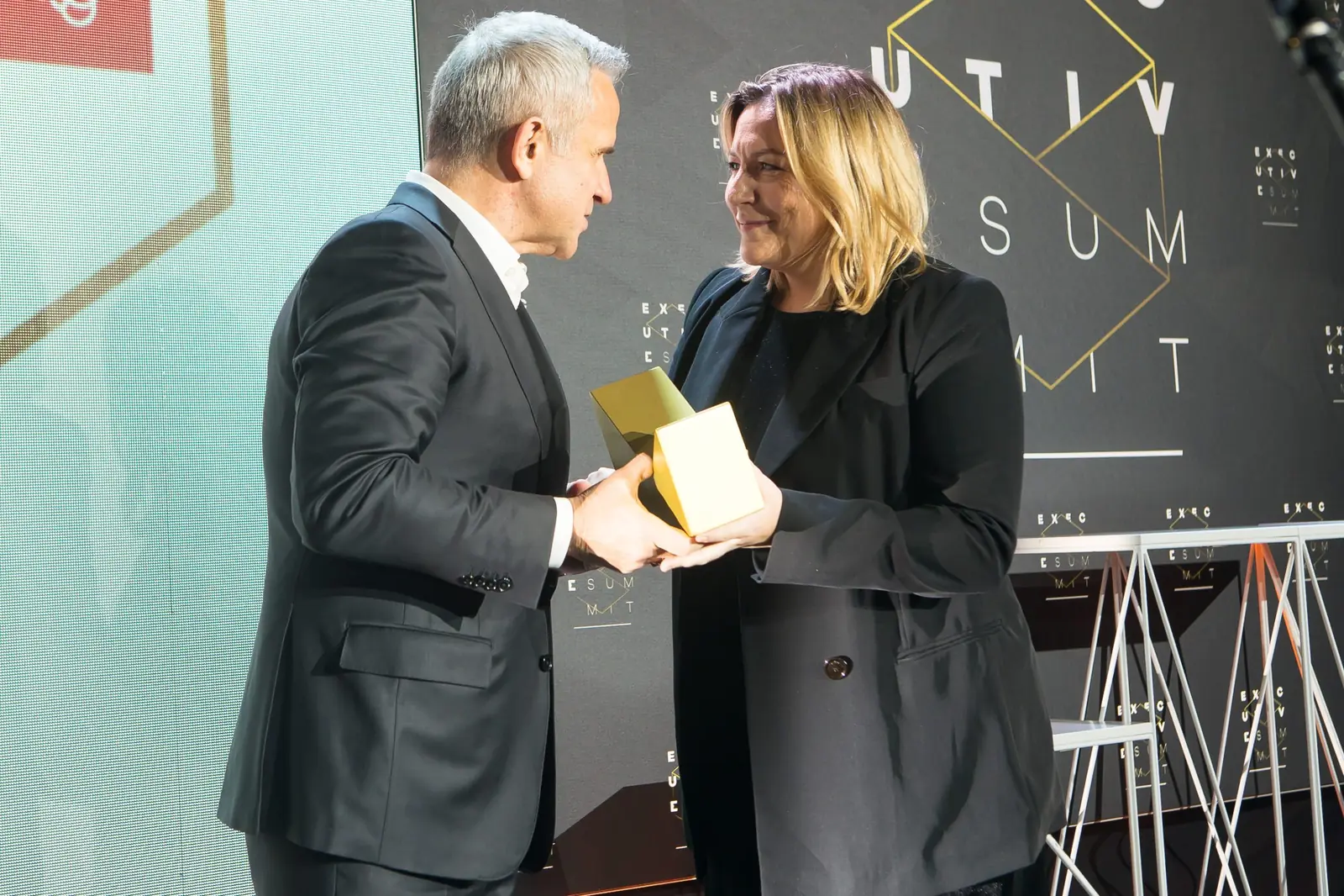 Laureatka w czarnym żakiecie przejmuje statuetkę z rąk szpakowatego wręczającego — Gala DMR XI (2022)