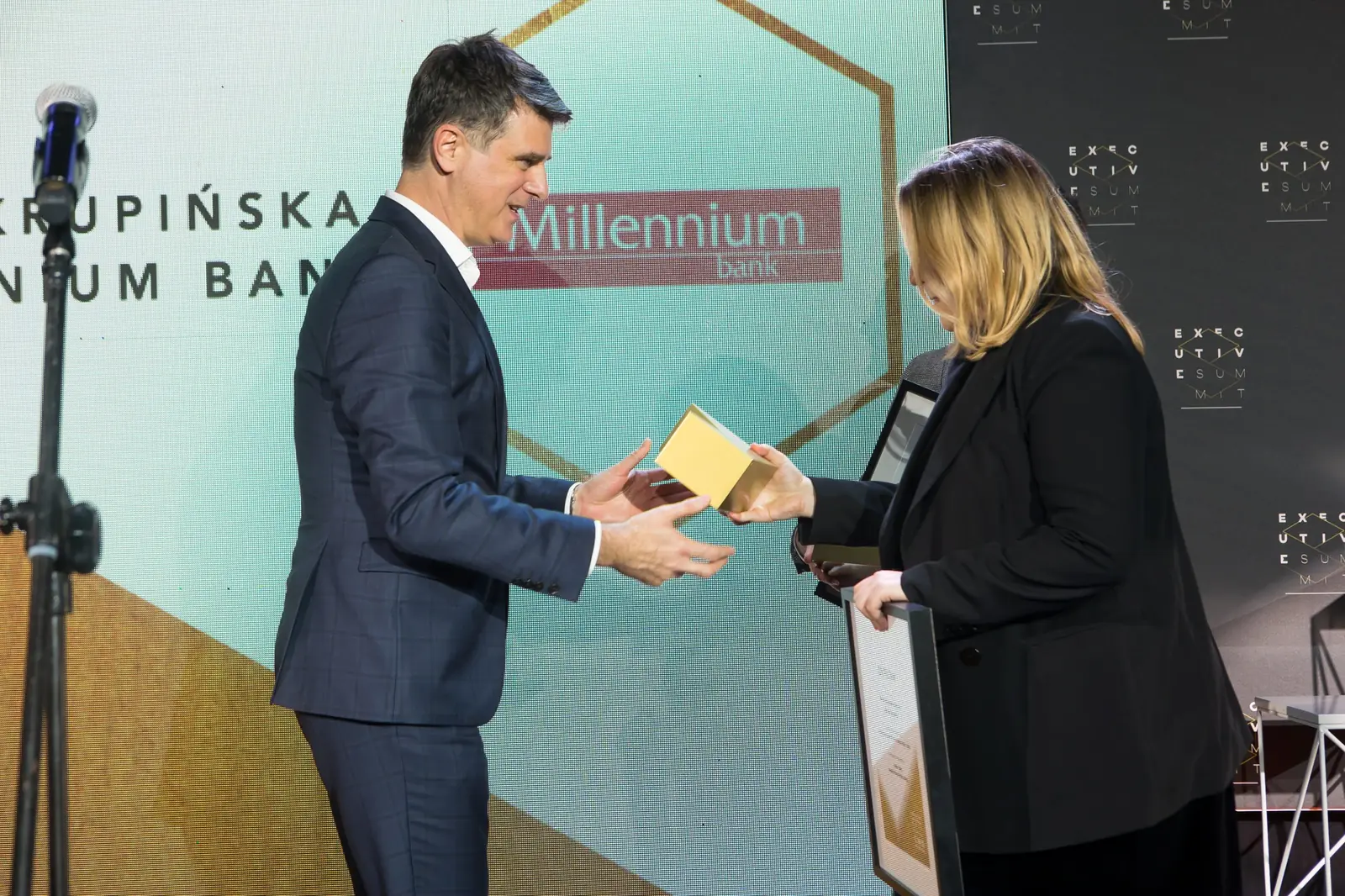 Mężczyzna w granatowym garniturze podaje złotą statuetkę laureatce trzymającej już dyplom — Gala DMR XI (2022)