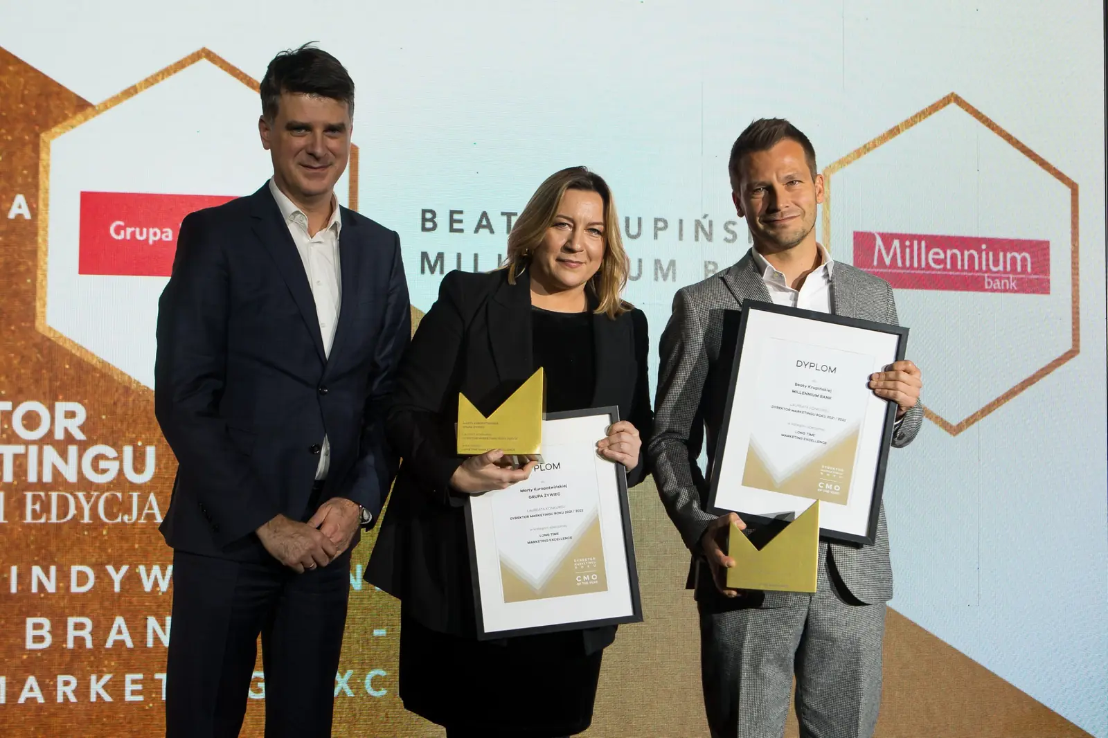 Laureatka w czerni i laureat w szarym garniturze prezentują dyplomy, obok stoi wręczający — Gala DMR XI (2022)