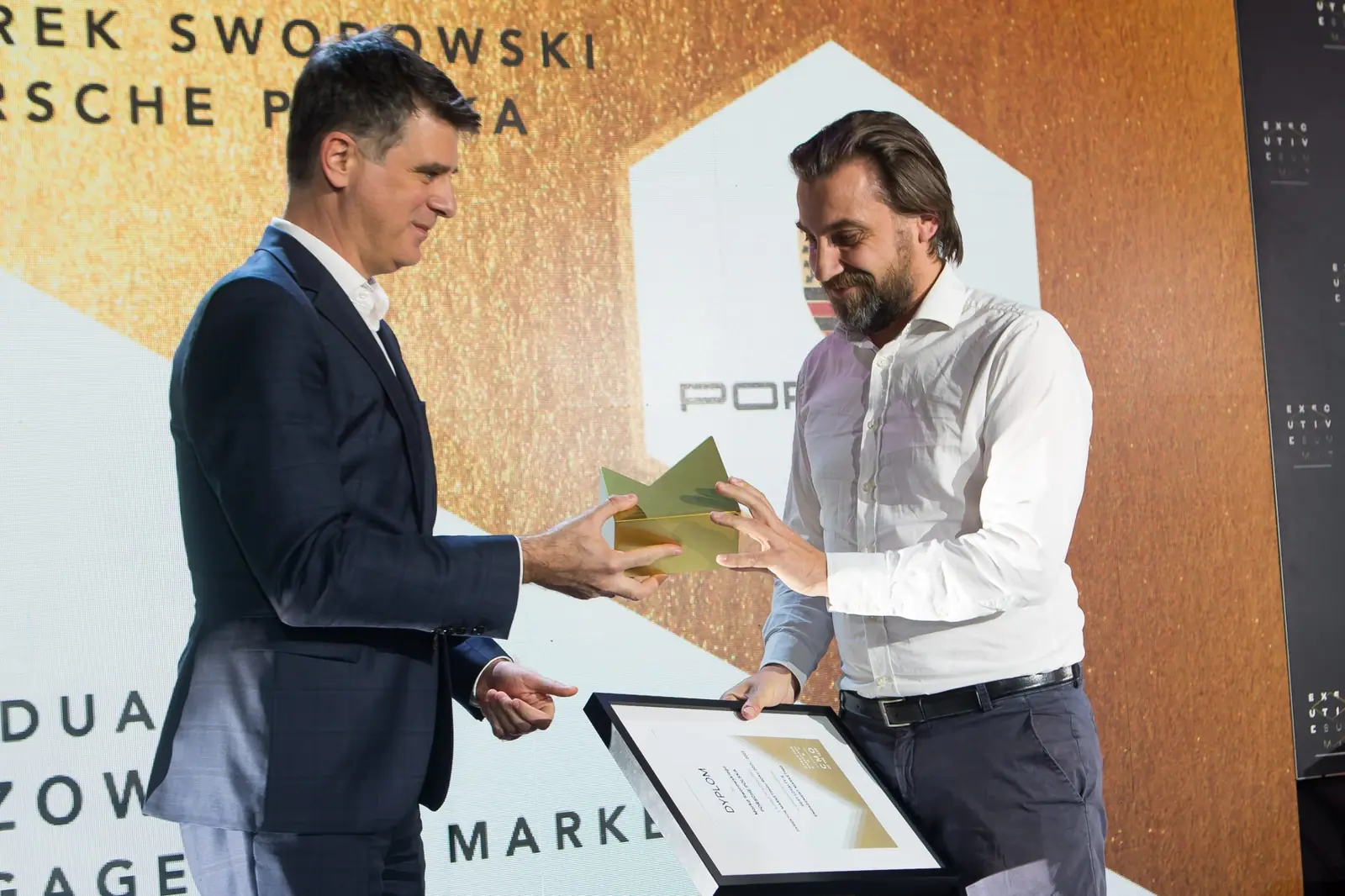 Laureat w białej koszuli z dyplomem odbiera statuetkę od mężczyzny w granatowym garniturze — Gala DMR XI (2022)