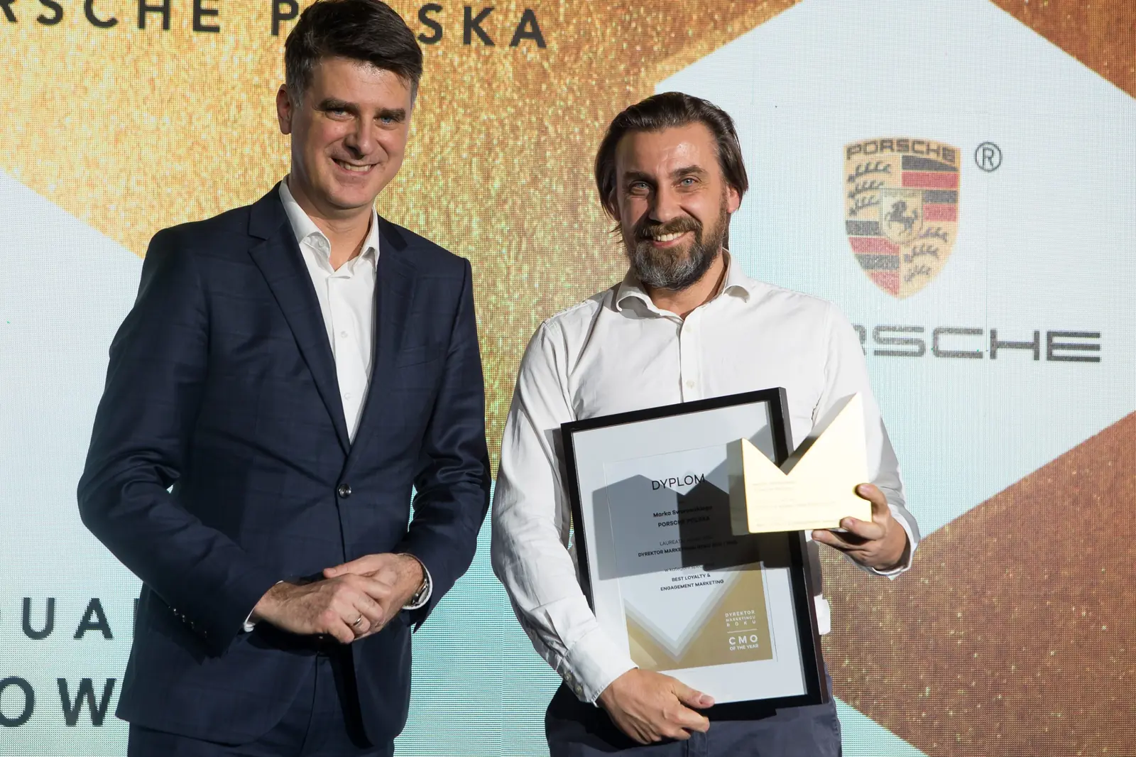 Oficjalne zdjęcie: brodaty laureat w rozpiętej białej koszuli z nagrodami i wręczający w garniturze — Gala DMR XI (2022)