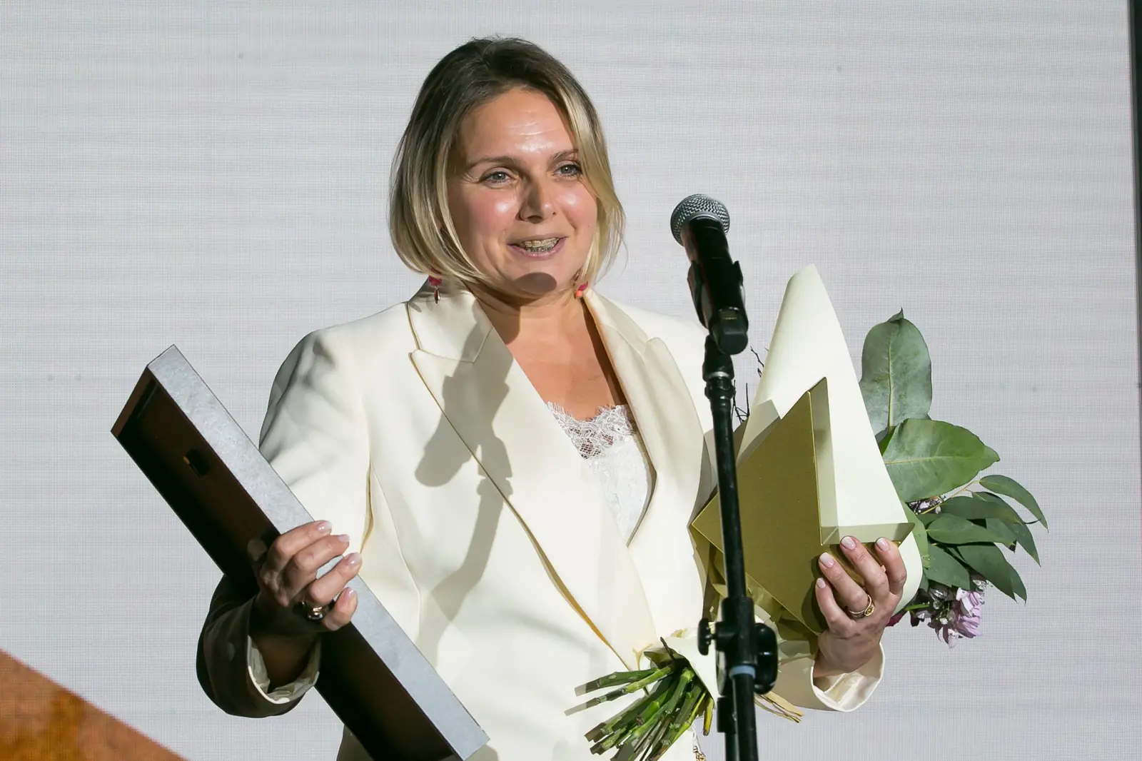 Laureatka w kremowym garniturze przemawia z kwiatami, dyplomem i statuetką w dłoniach — Gala DMR XI (2022)
