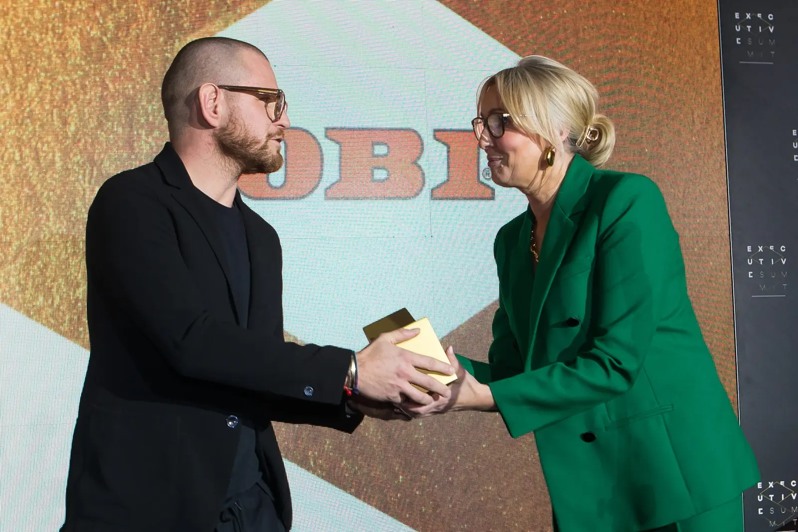 Kobieta w zielonym garniturze i mężczyzna w czerni wspólnie trzymają złotą statuetkę — Gala DMR XI (2022)