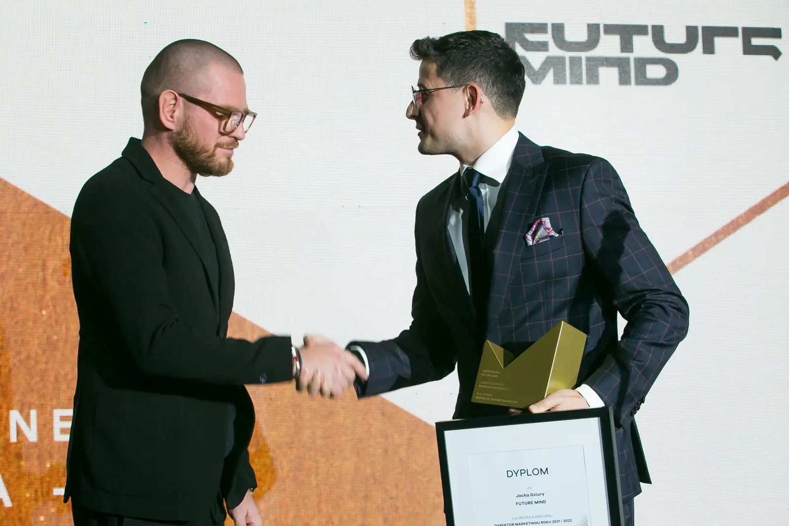Laureat w garniturze w kratę z poszetką ściska dłoń wręczającego po odbiorze dyplomu — Gala DMR XI (2022)