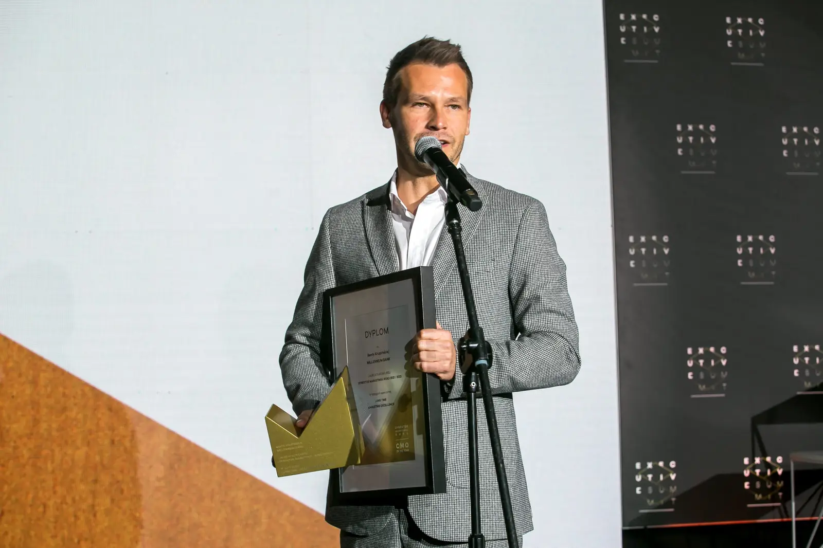 Laureat w szarym garniturze dziękuje, trzymając dyplom w jednej, a statuetkę w drugiej ręce — Gala DMR XI (2022)