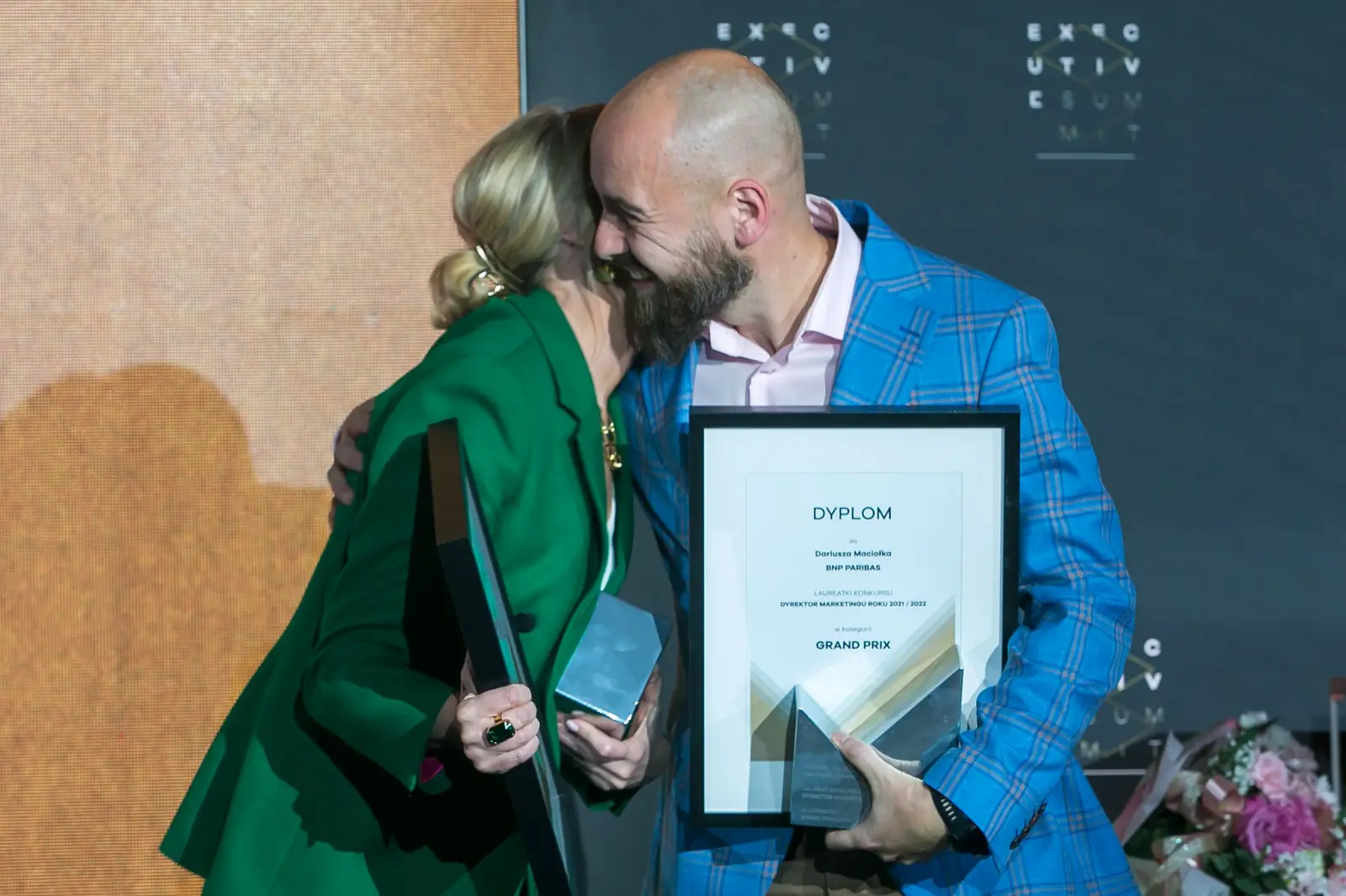 Kobieta w zieleni przytula laureata w niebieskiej marynarce trzymającego dyplom Grand Prix — Gala DMR XI (2022)