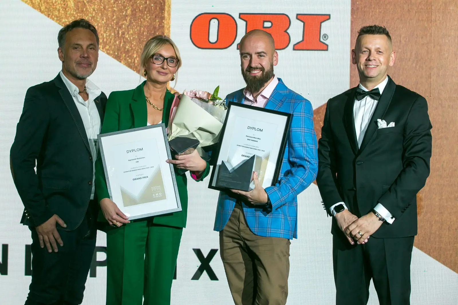 Dwoje laureatów Grand Prix z dyplomami i kwiatami w otoczeniu prowadzących gali — Gala DMR XI (2022)