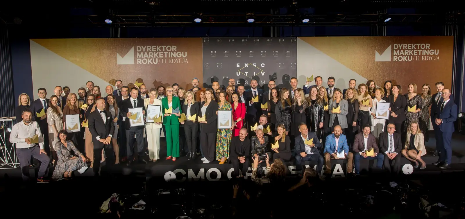 Kilkudziesięciu laureatów ze statuetkami i dyplomami na pamiątkowym zdjęciu na scenie — Gala DMR XI (2022)