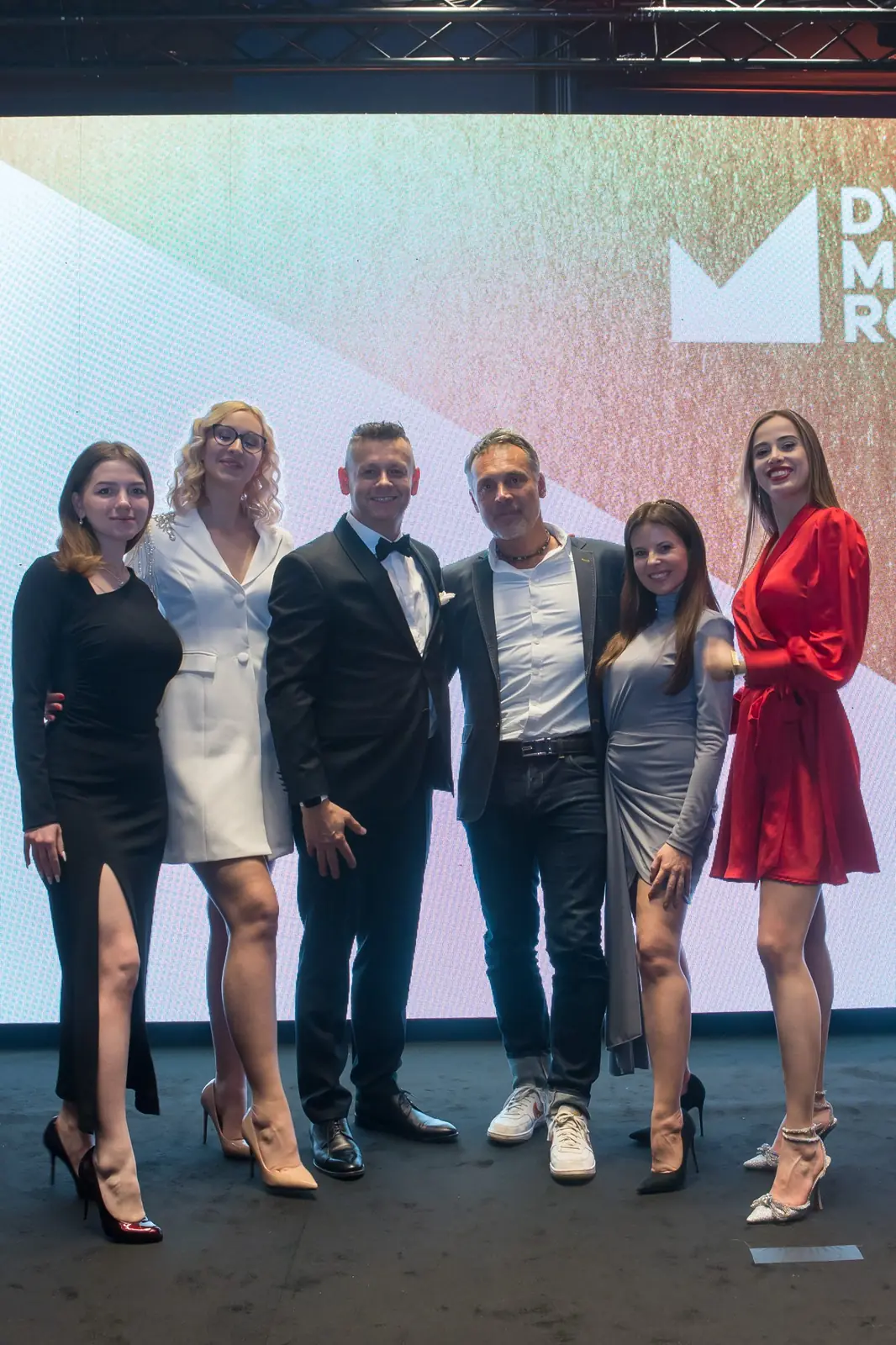 Sześcioro gości w wieczorowych strojach pozuje przed kolorową ścianką z logo konkursu — Gala DMR XI (2022)