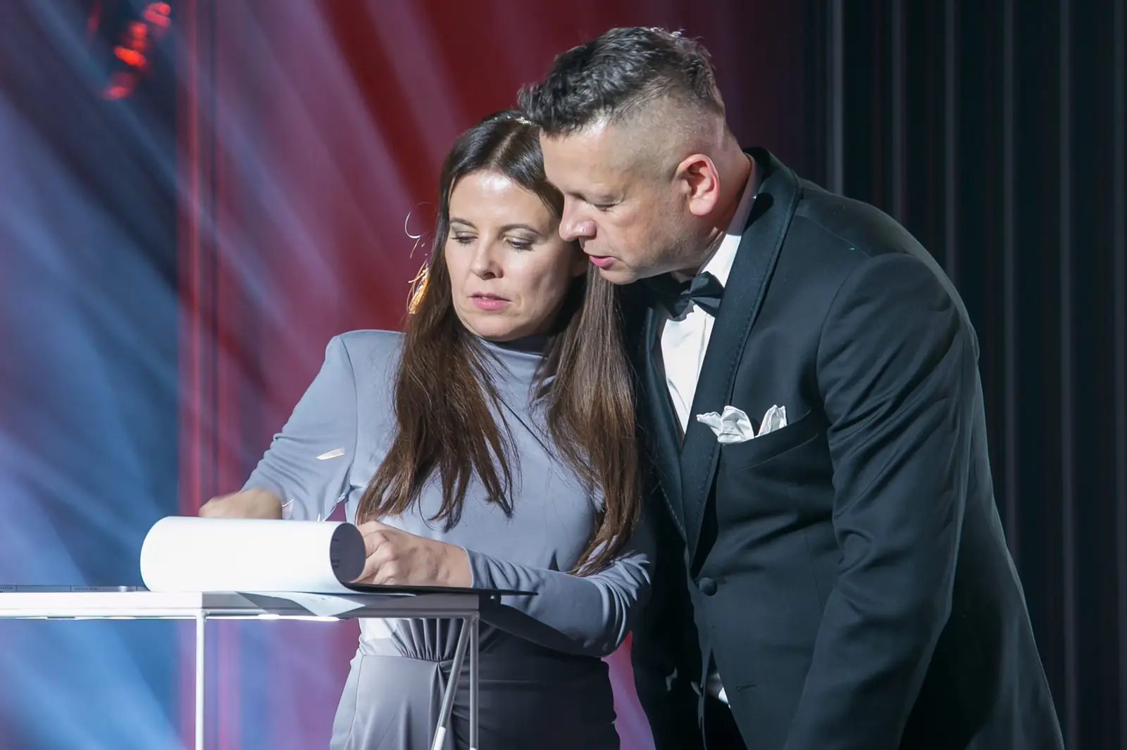 Prowadzący pochyla się nad scenariuszem gali razem z kobietą w szarej sukience — Gala DMR XI (2022)