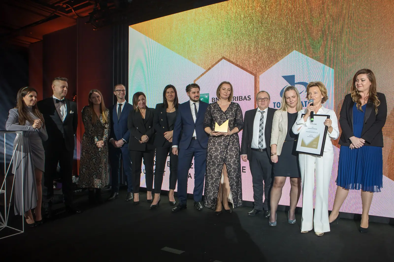 Laureatka w białym garniturze przemawia w imieniu licznej grupy stojącej na scenie — Gala DMR XI (2022)