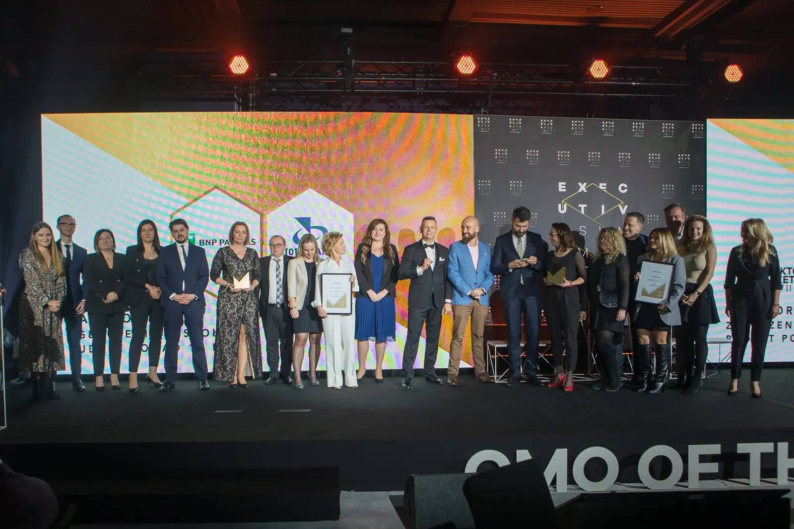 Dwie grupy laureatów łączą się we wspólnym zdjęciu na scenie pod czerwonymi reflektorami — Gala DMR XI (2022)