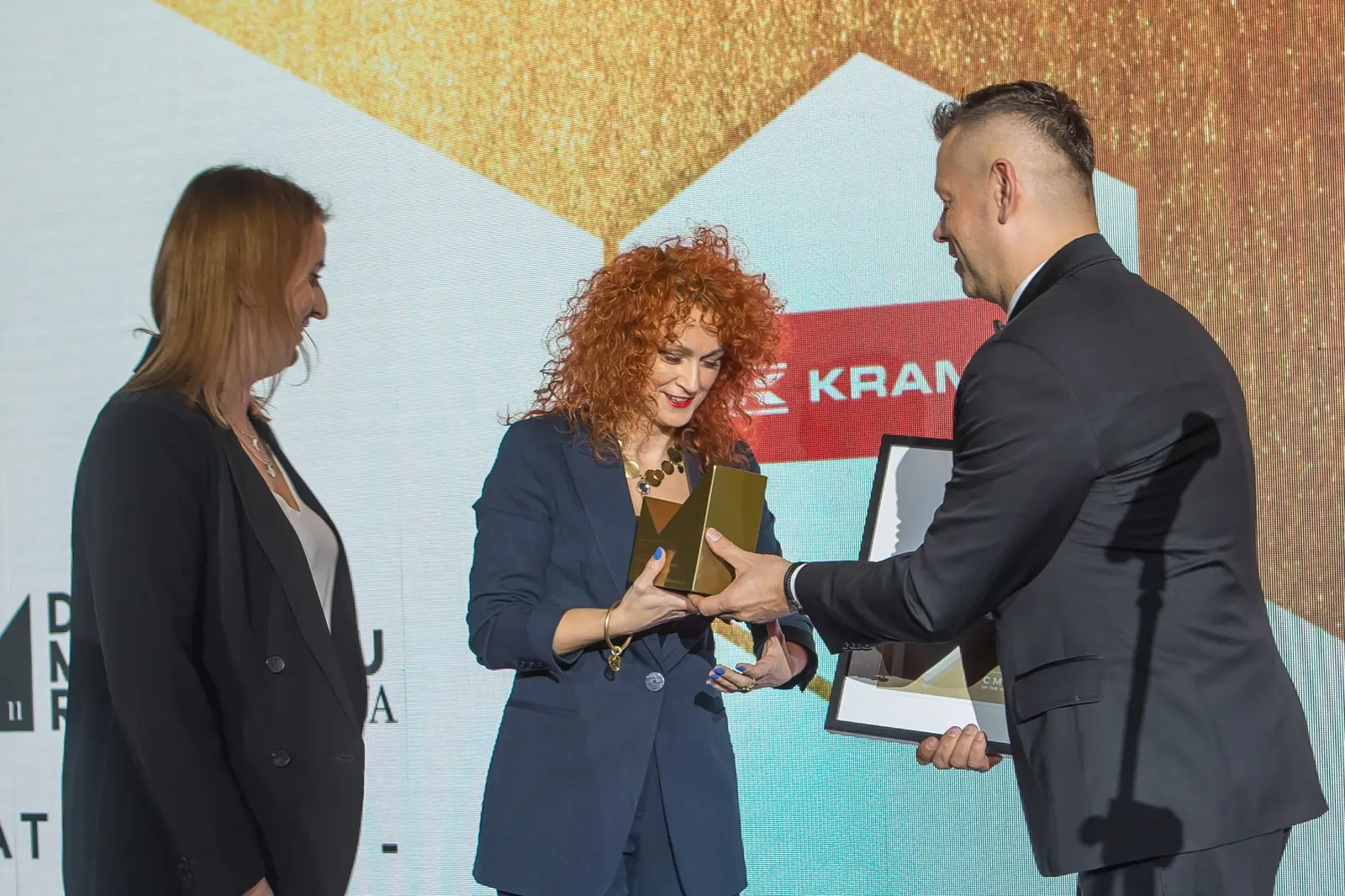 Wręczający przekazuje statuetkę rudowłosej laureatce, obok stoi kobieta w czarnym żakiecie — Gala DMR XI (2022)