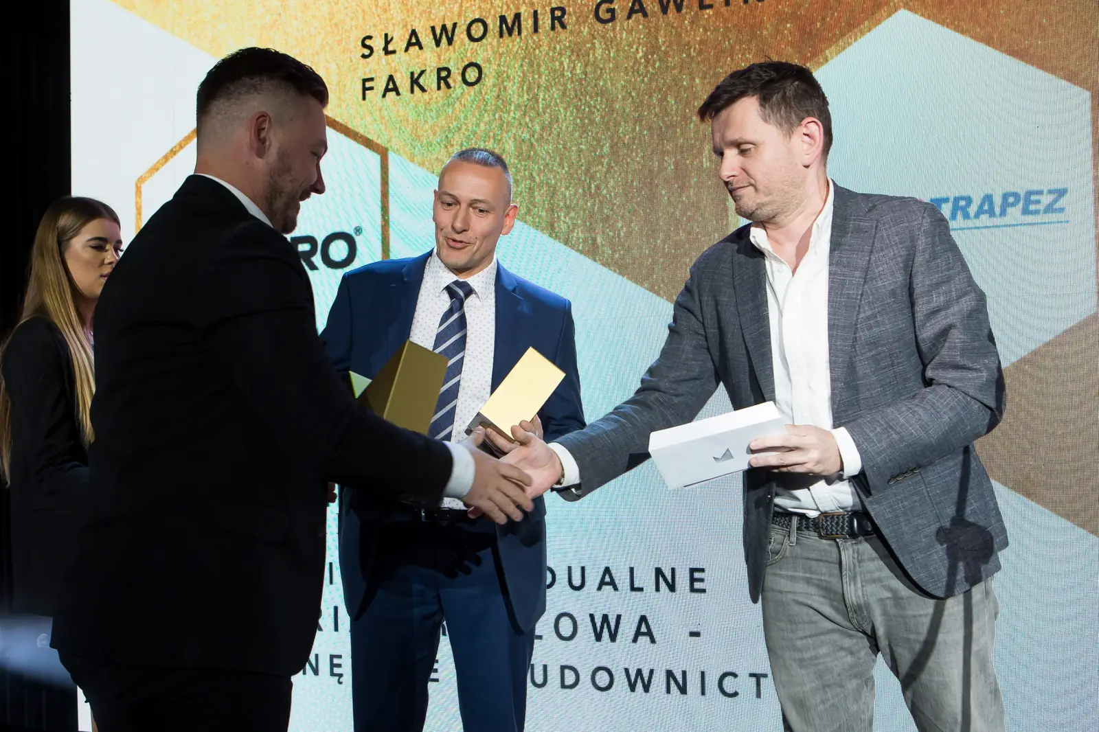 Mężczyzna w czerni gratuluje laureatowi w granatowym garniturze, obok wręczający z kopertą — Gala DMR XI (2022)