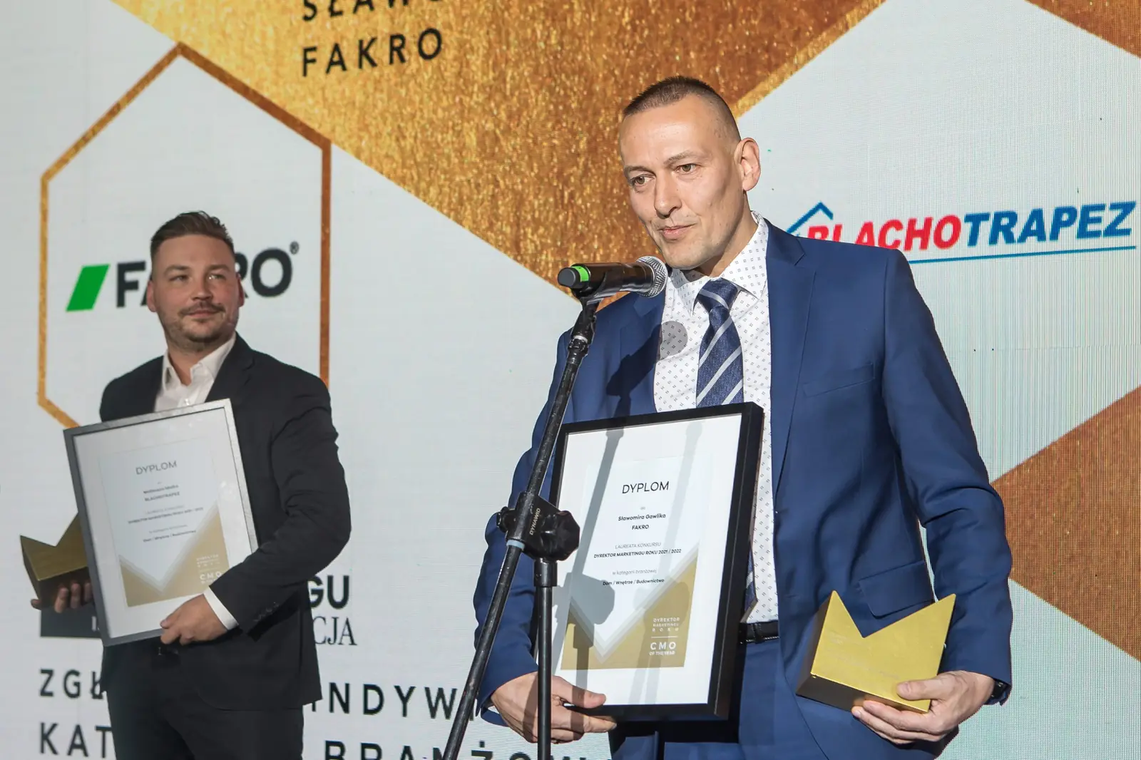 Laureat w krawacie w paski przemawia z dyplomem i statuetką, obok kolega z dyplomem — Gala DMR XI (2022)