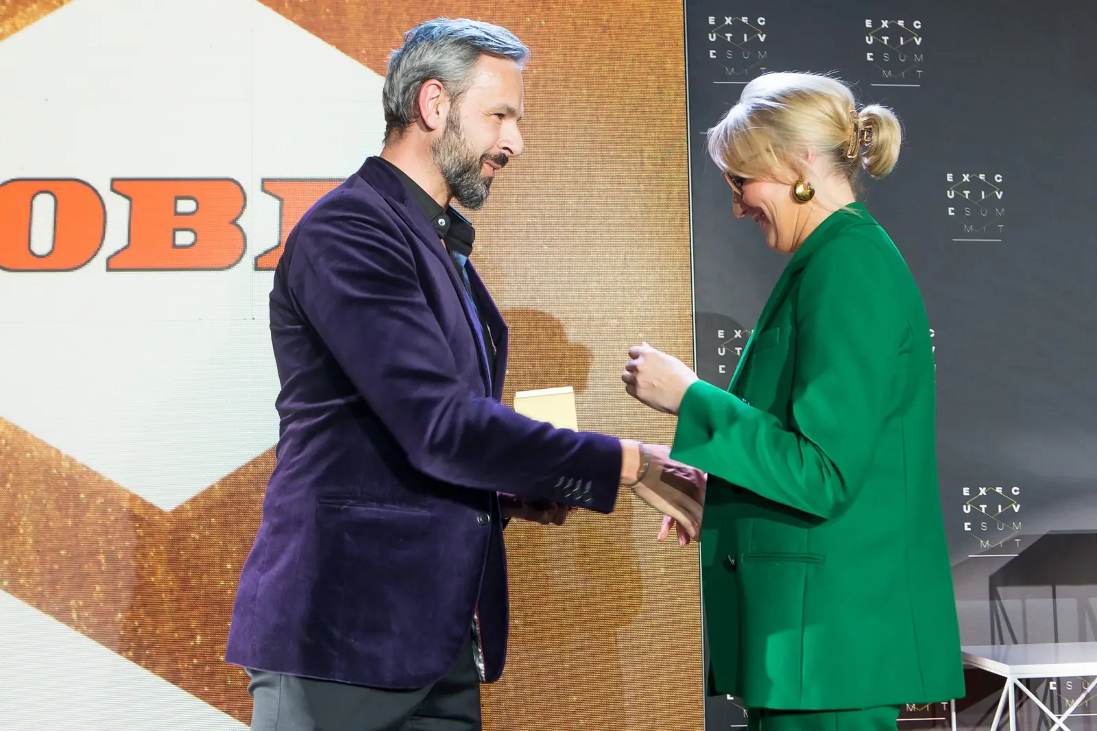 Laureatka z upiętymi włosami w zielonym garniturze wita się z mężczyzną w fioletowej marynarce — Gala DMR XI (2022)
