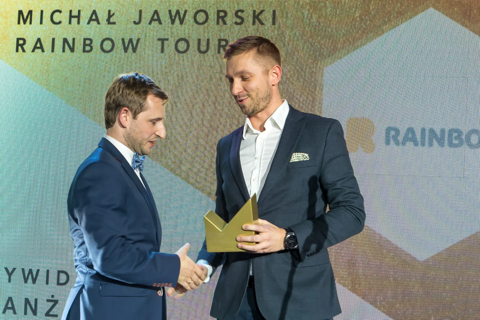 Laureat z muszką ściska dłoń wręczającego, trzymając złotą statuetkę w drugiej ręce — Gala DMR XI (2022)