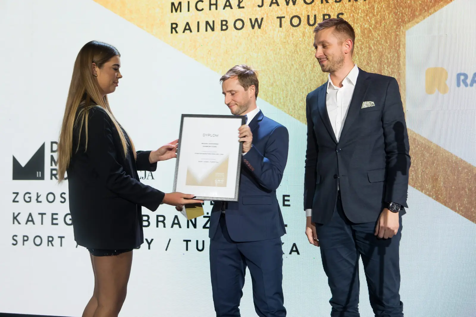Asystentka podaje oprawiony dyplom laureatowi z muszką, obok stoi wręczający — Gala DMR XI (2022)
