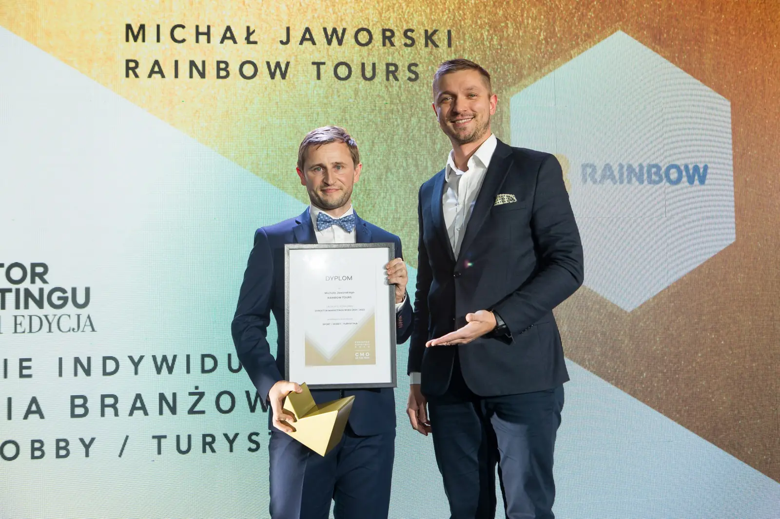 Laureat z muszką pozuje z dyplomem i statuetką, a wręczający wskazuje go dłonią — Gala DMR XI (2022)