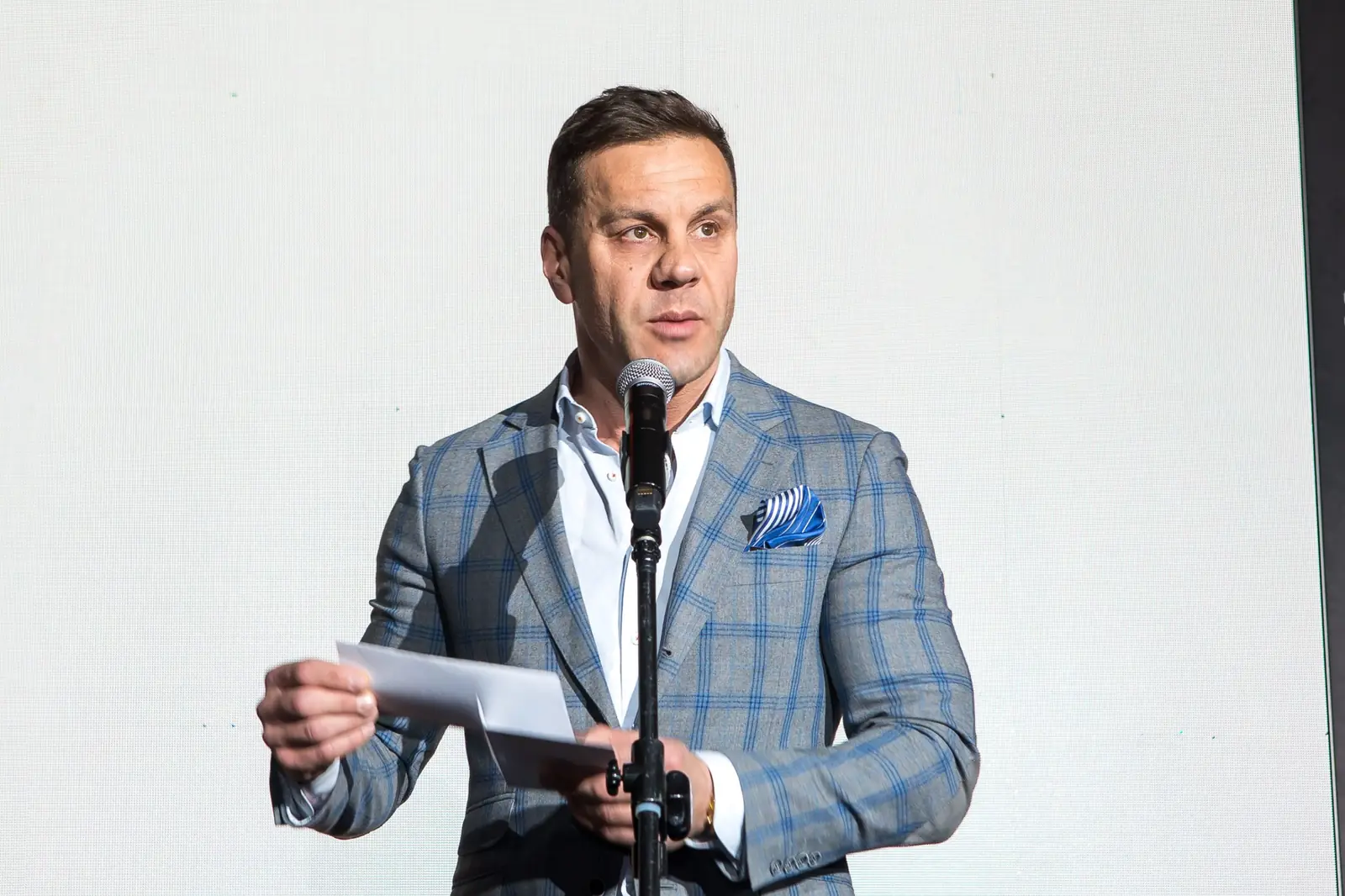 Wręczający w szarej marynarce w kratę odczytuje werdykt z koperty przy mikrofonie — Gala DMR XI (2022)