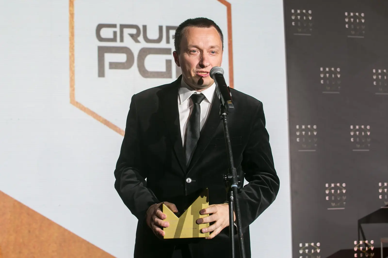 Laureat w czarnym garniturze uśmiecha się przy mikrofonie, trzymając statuetkę w obu dłoniach — Gala DMR XI (2022)