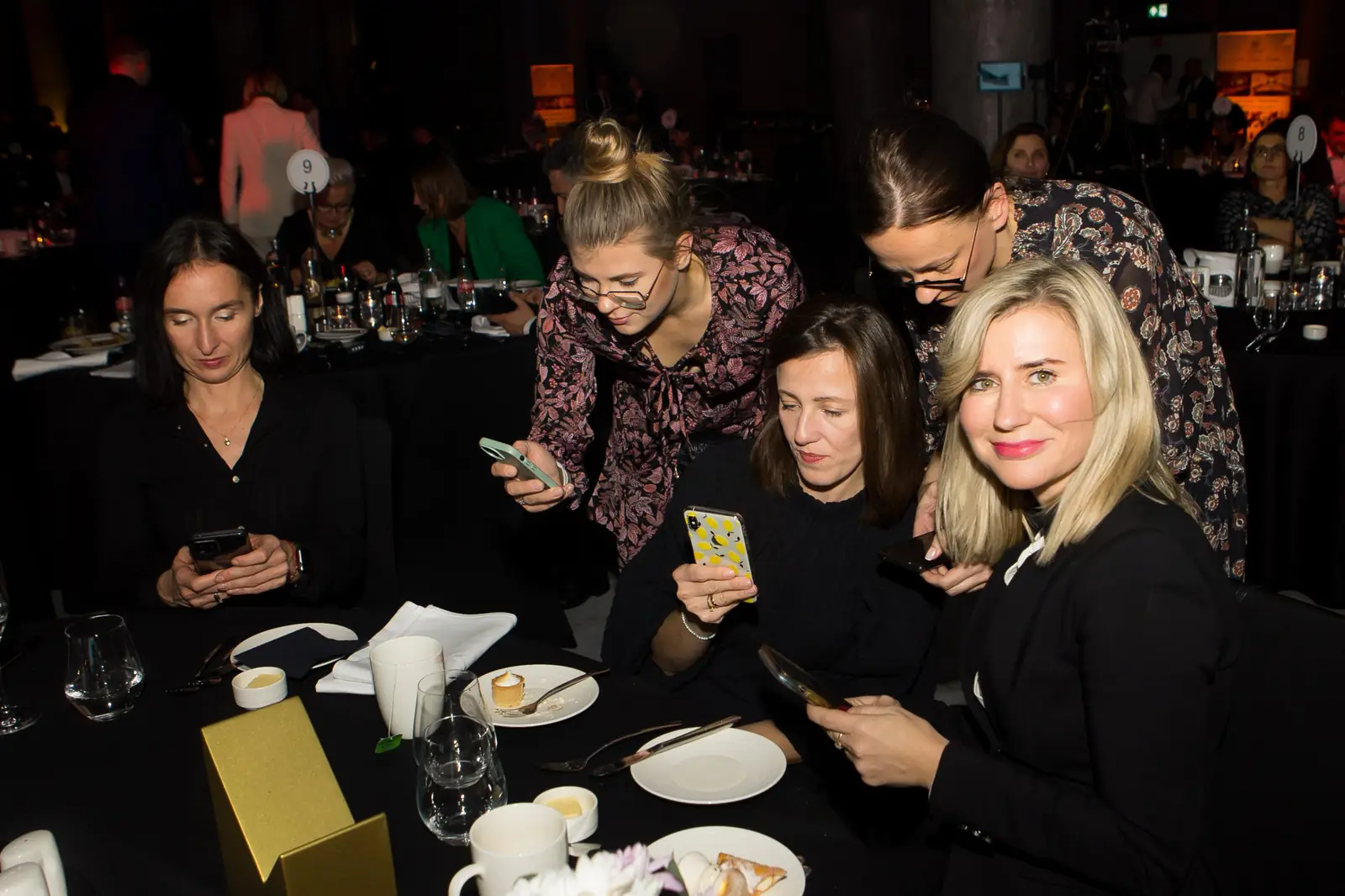 Kobiety przy stoliku przeglądają zdjęcia w telefonach, na obrusie stoi złota statuetka — Gala DMR XI (2022)