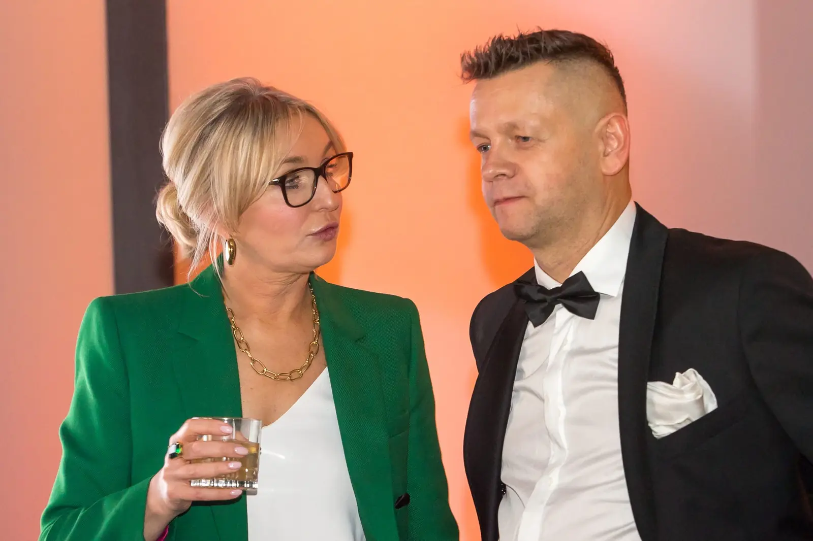 Laureatka w zielonym żakiecie ze szklanką w dłoni rozmawia z prowadzącym w smokingu — Gala DMR XI (2022)