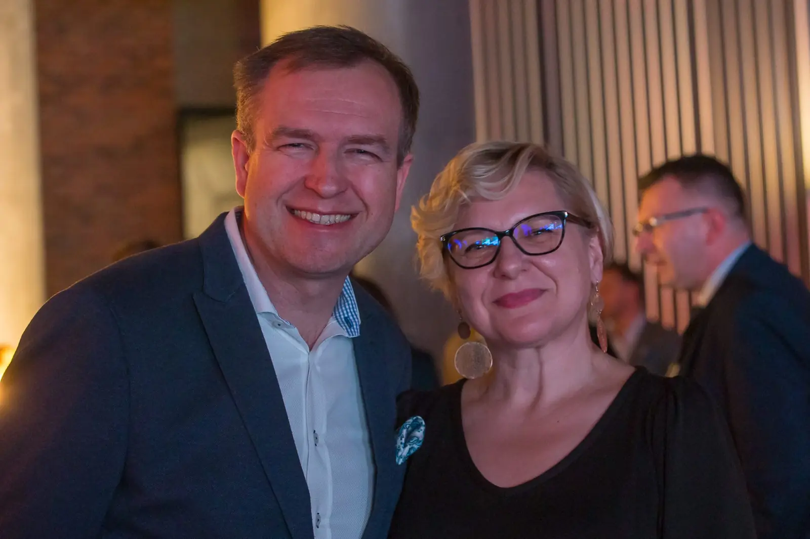 Uśmiechnięty mężczyzna w granatowej marynarce i kobieta w okularach pozują w sali — Gala DMR XI (2022)